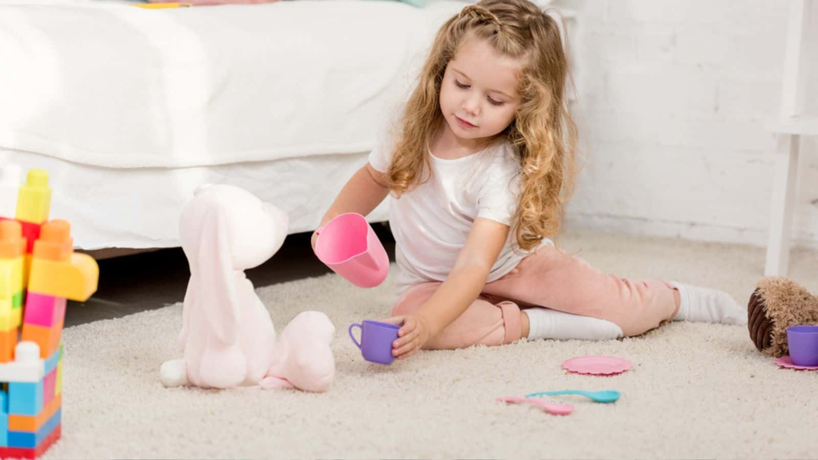 Adorable little girl playing with rabbit toy and plastic cups in children room
