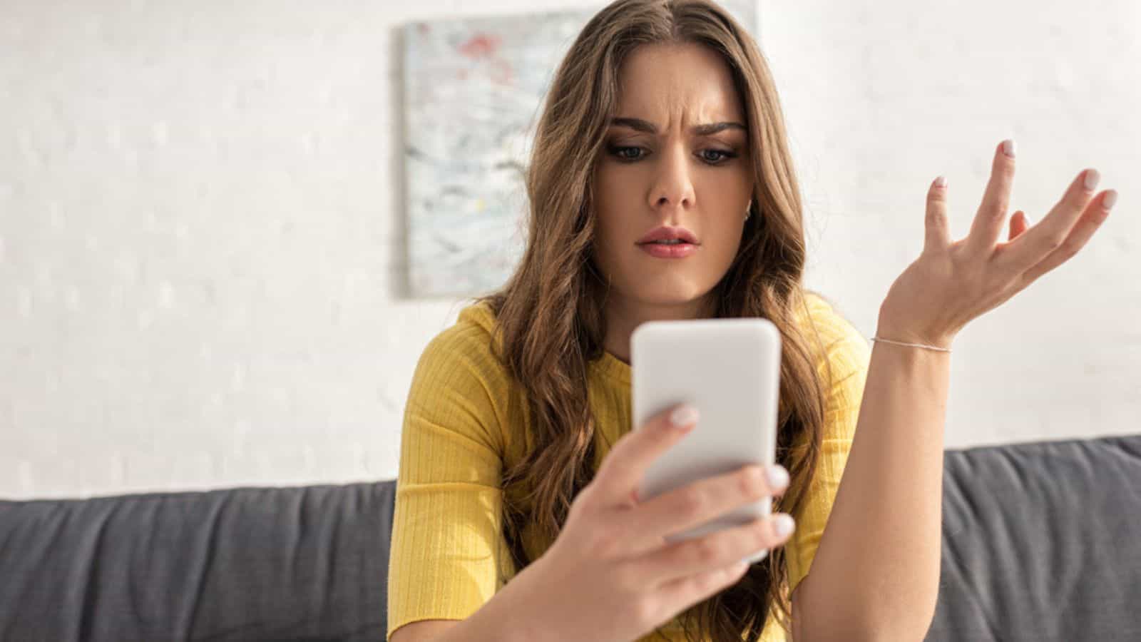 Attractive confused woman using smartphone on sofa in living room