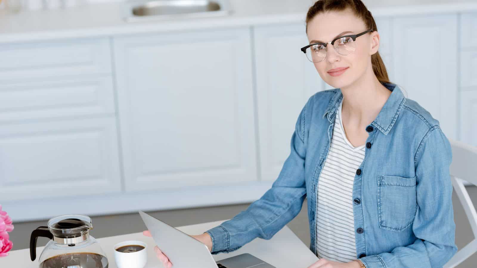 Attractive woman doing remote work on laptop on kitchen with coffee