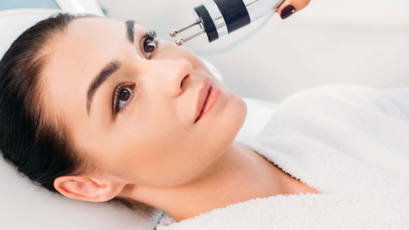 Attractive woman getting facial microcurrent therapy in spa salon