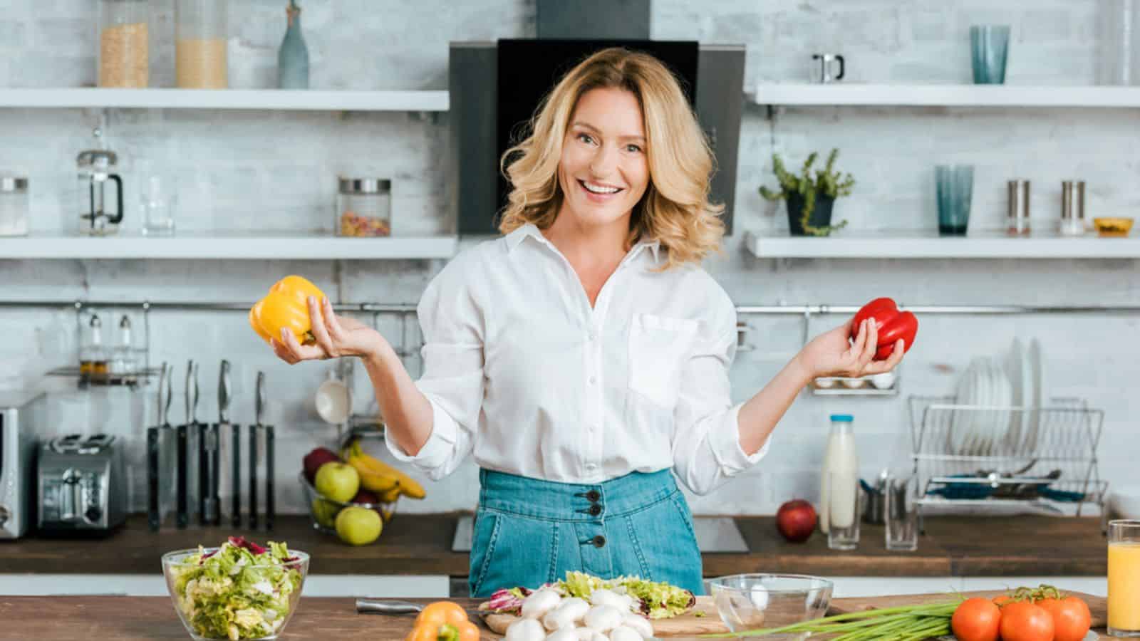Beautiful adult woman with bell peppers looking at camera while making salad at kitchen