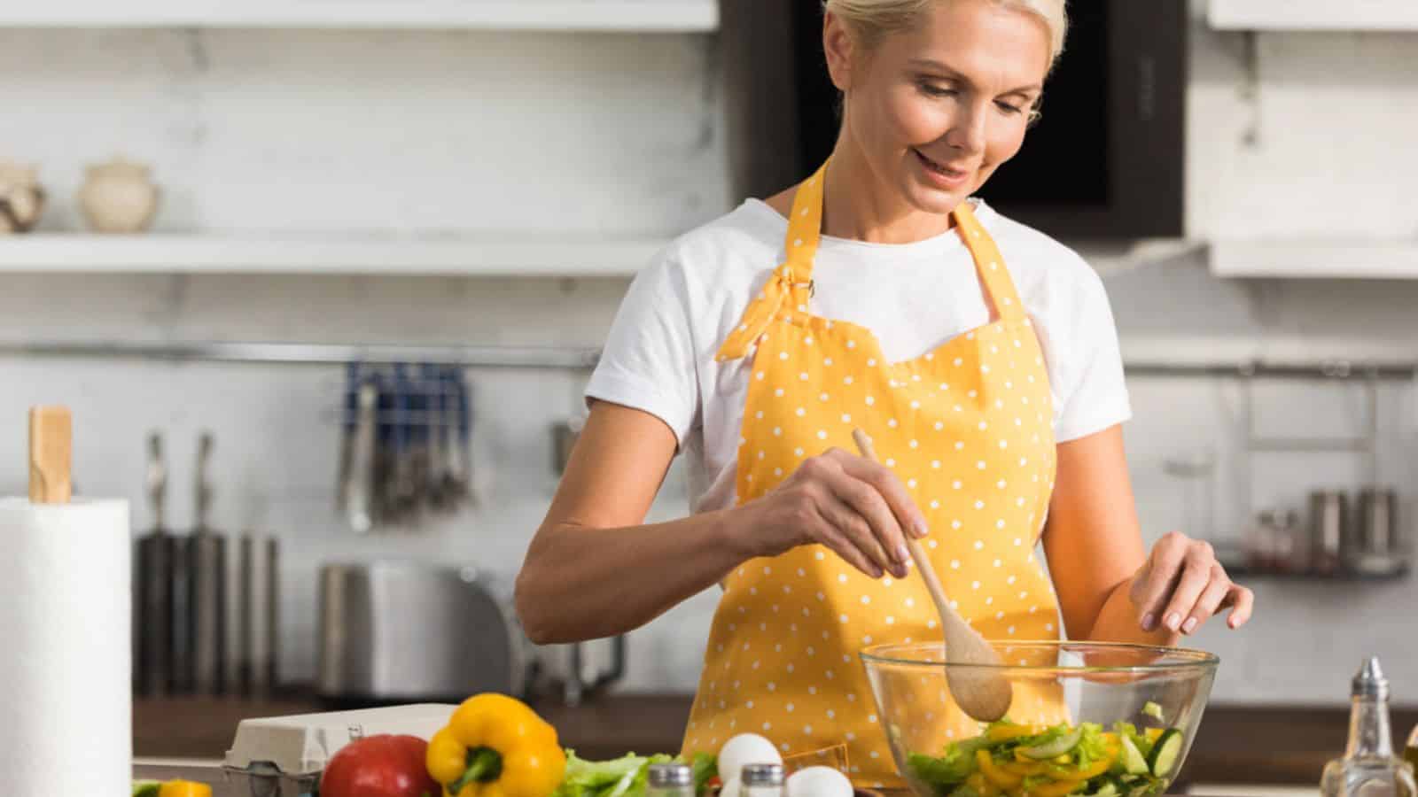 Beautiful happy mature woman in apron cooking vegetable salad