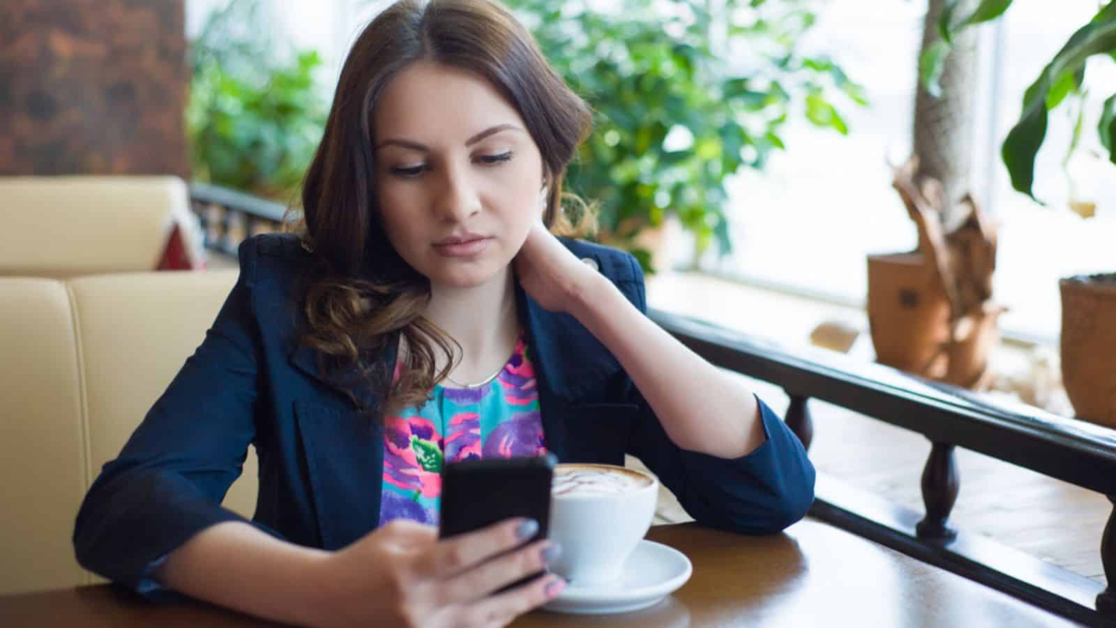 Beautiful young girl drinking coffee using her phone