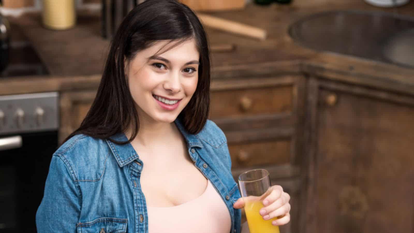 Beautiful young pregnant woman holding glass of fresh juice and smiling