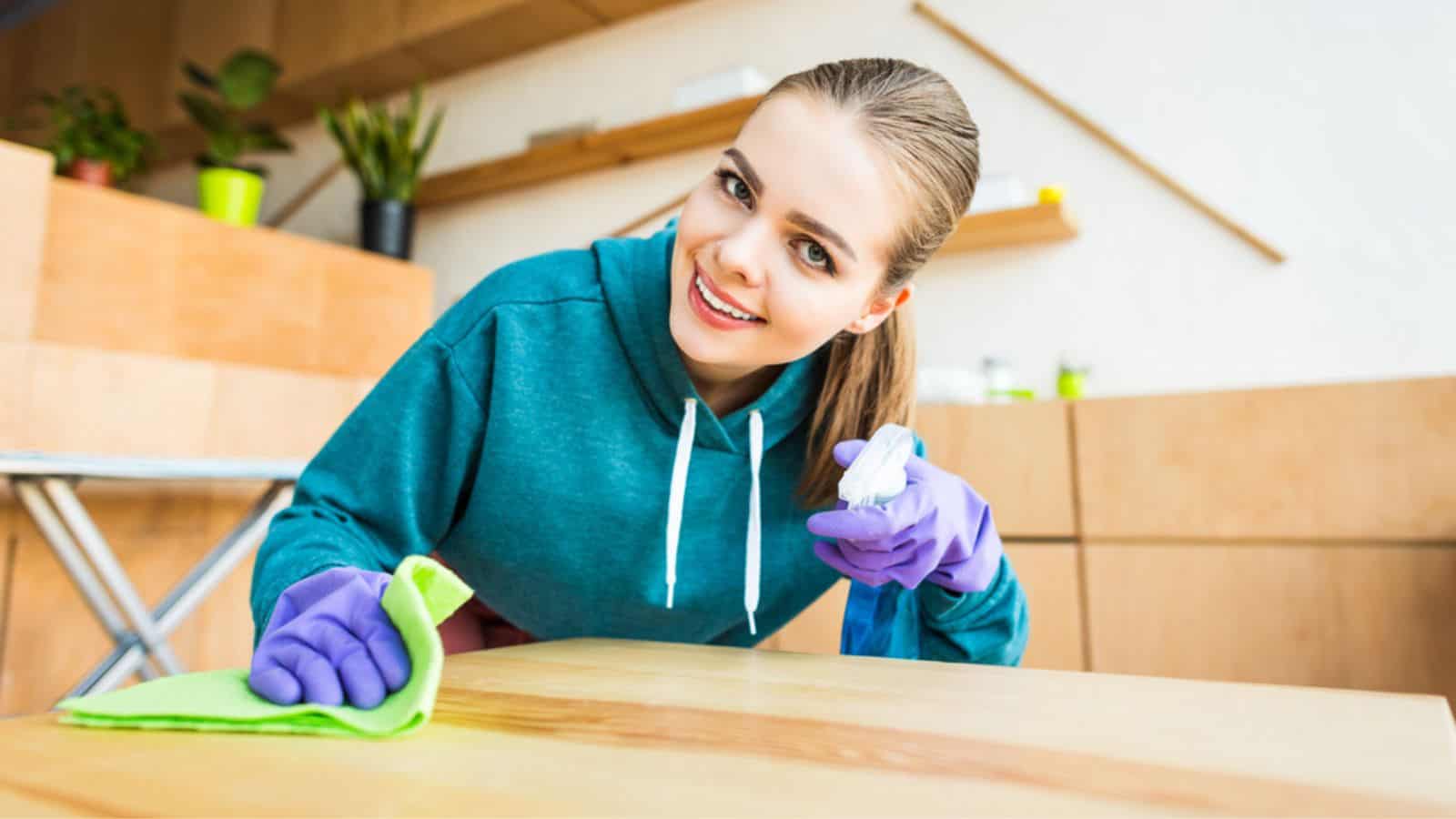 Beautiful young woman smiling at camera while cleaning home