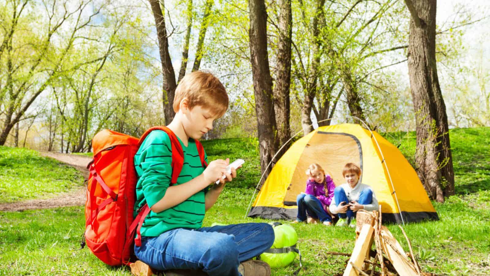 Boy with backpack writes notebook at camping