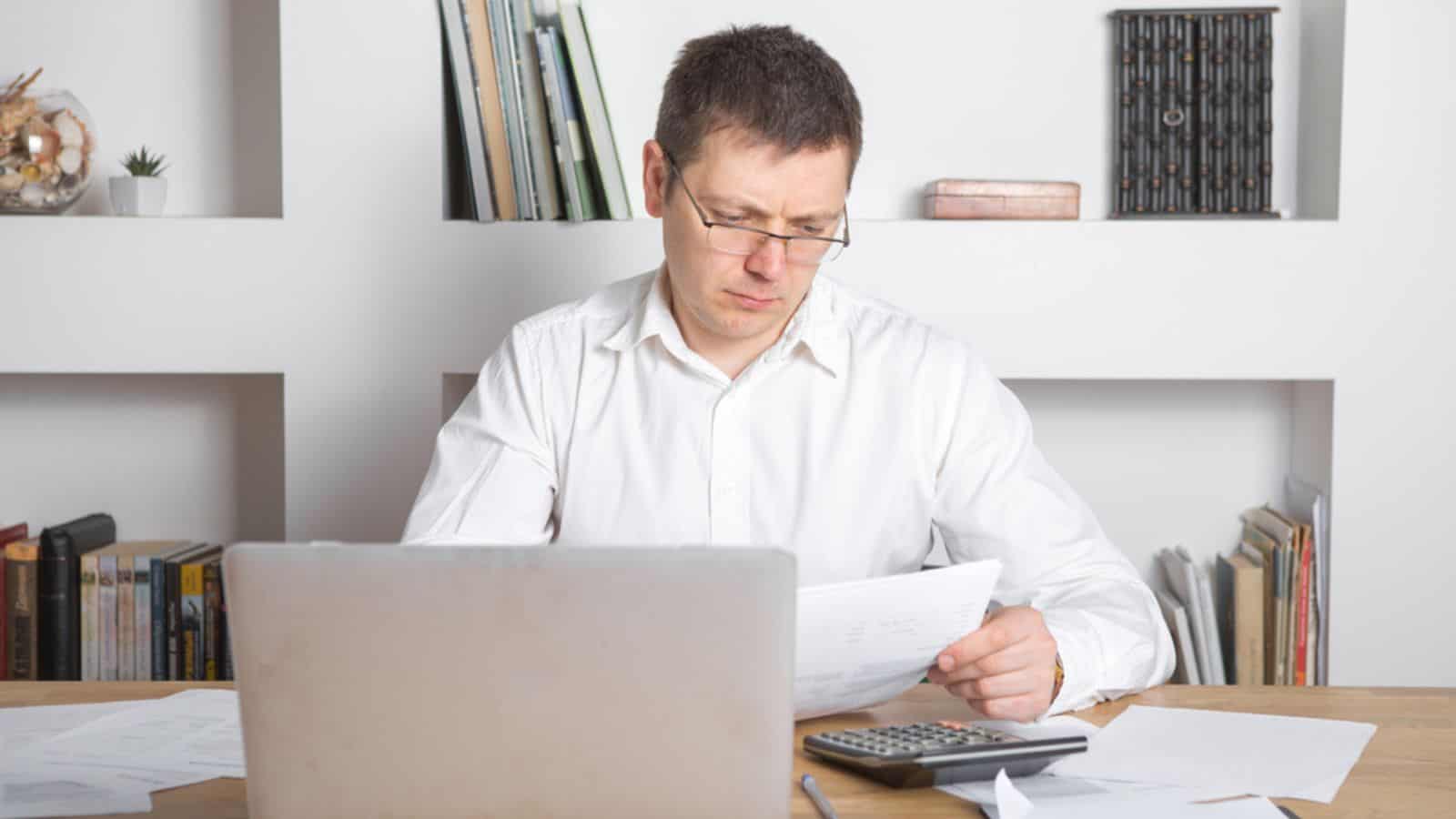 Businessman surprised and mad looking at the document with his calculator