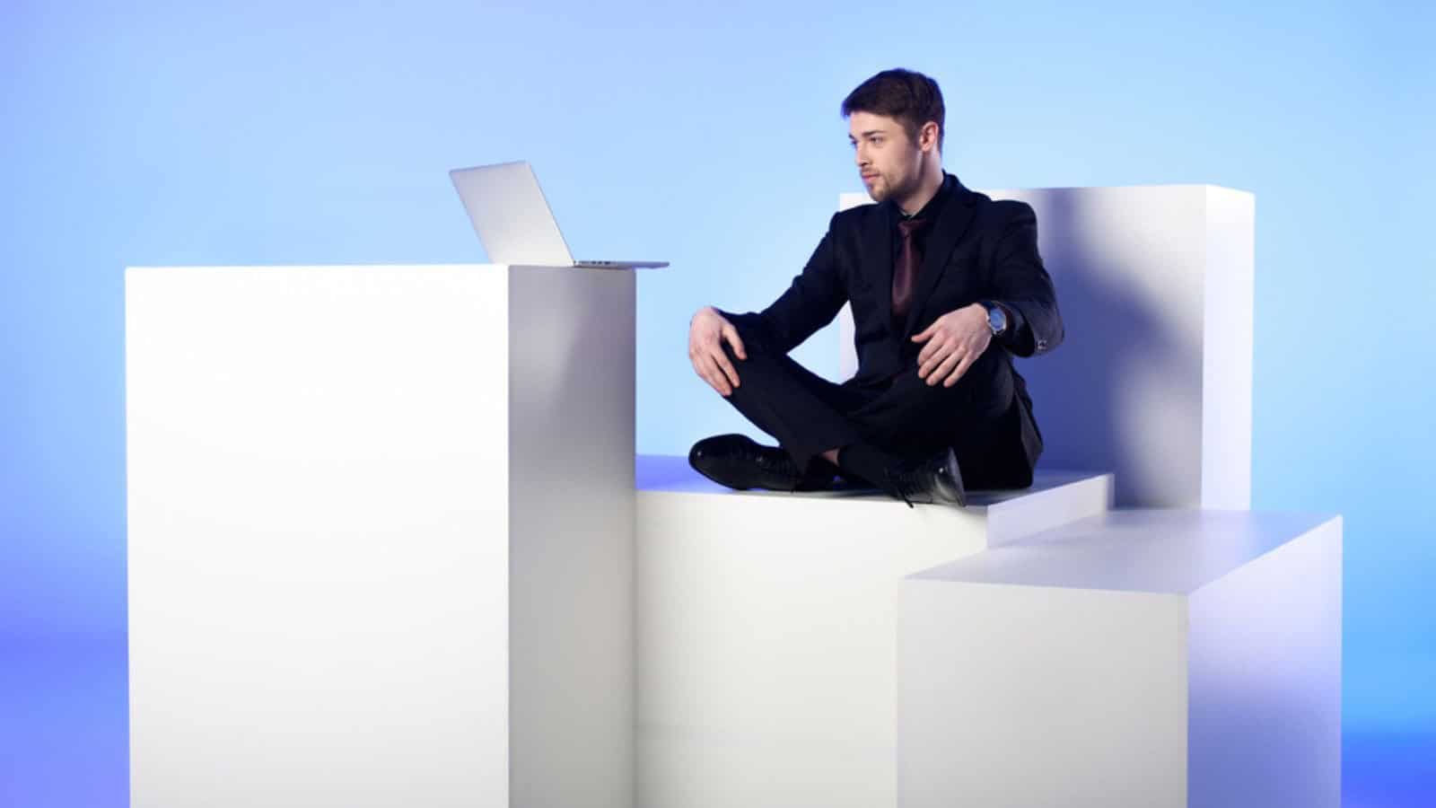 Businessman with laptop sitting on white block
