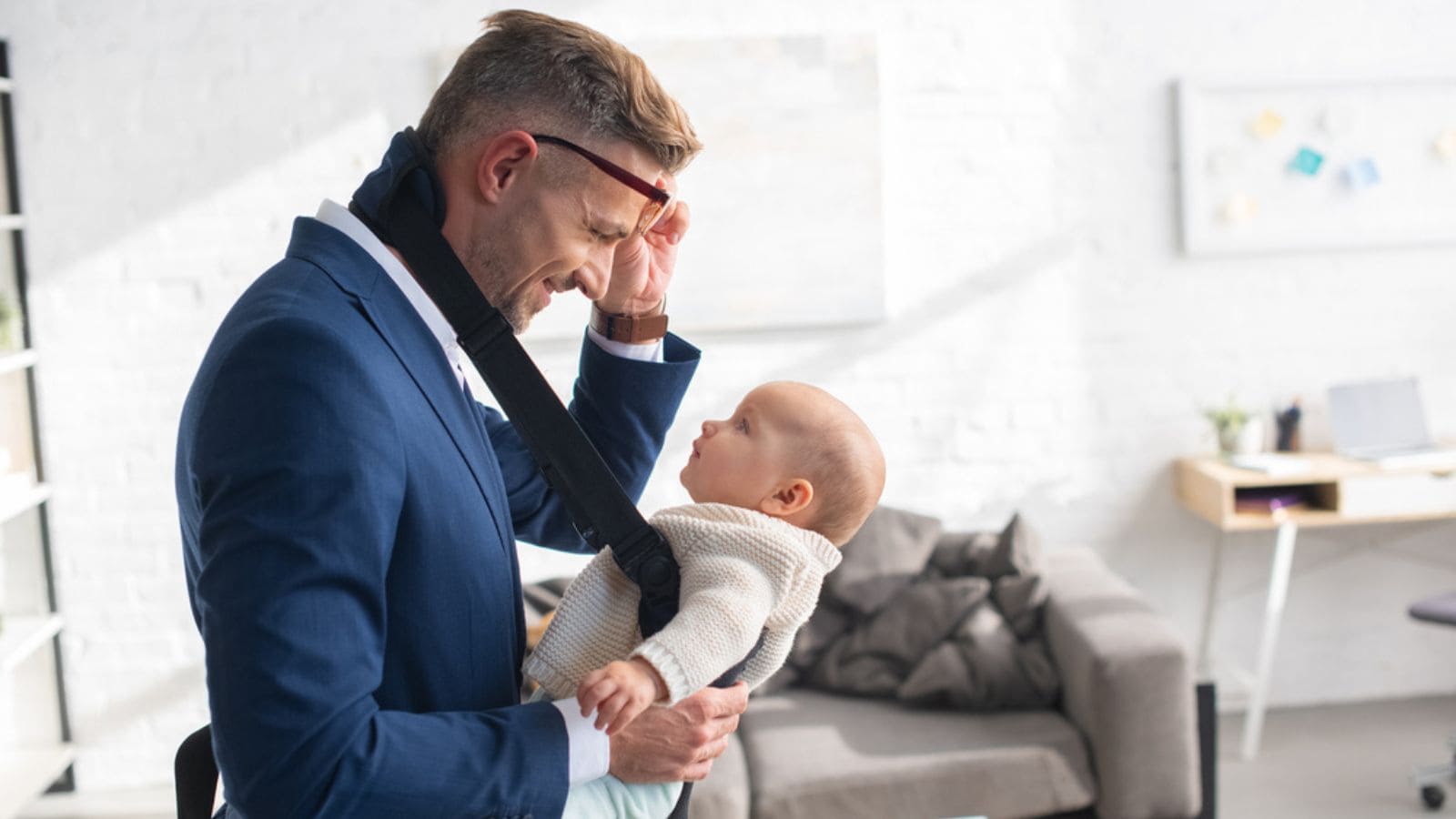 Cheerful businessman holding glasses and looking at infant