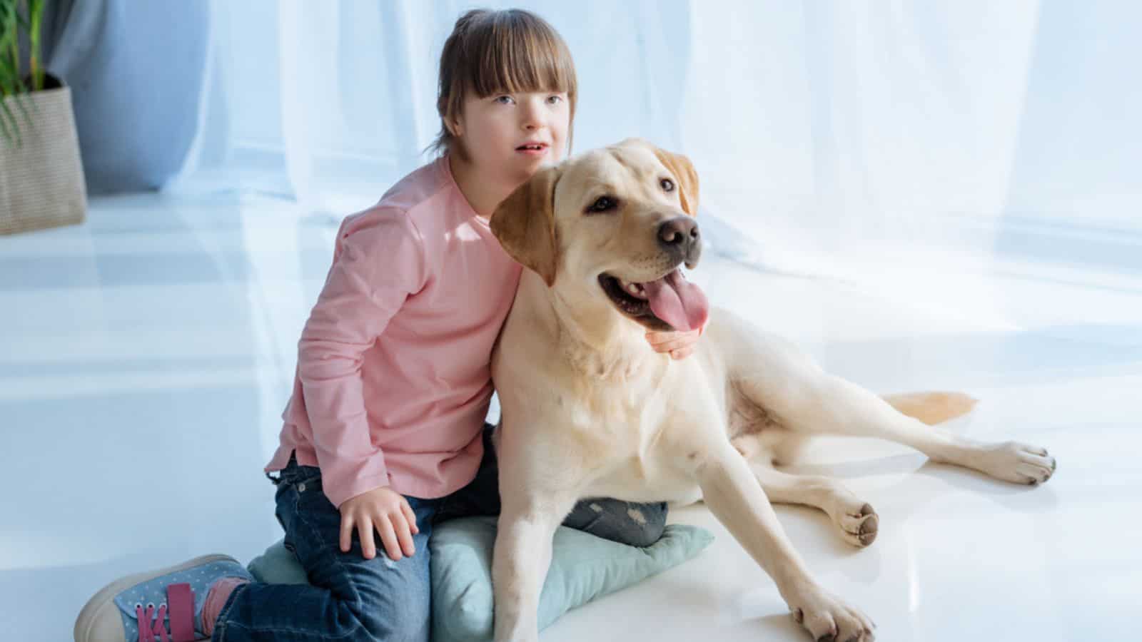 Child with down syndrome near Labrador dog on the floor