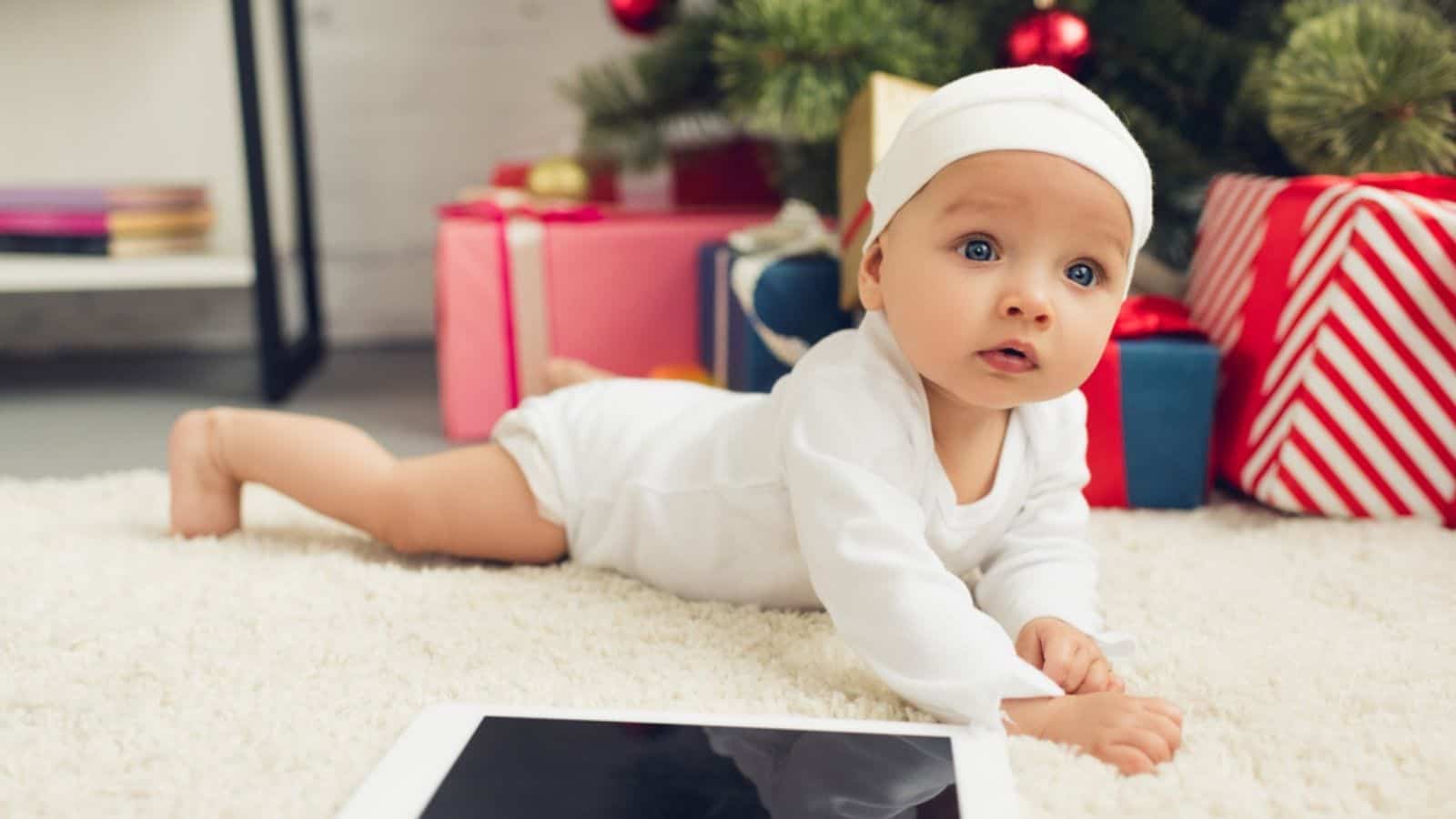 Close-up shot of beautiful little baby with tablet lying on floor