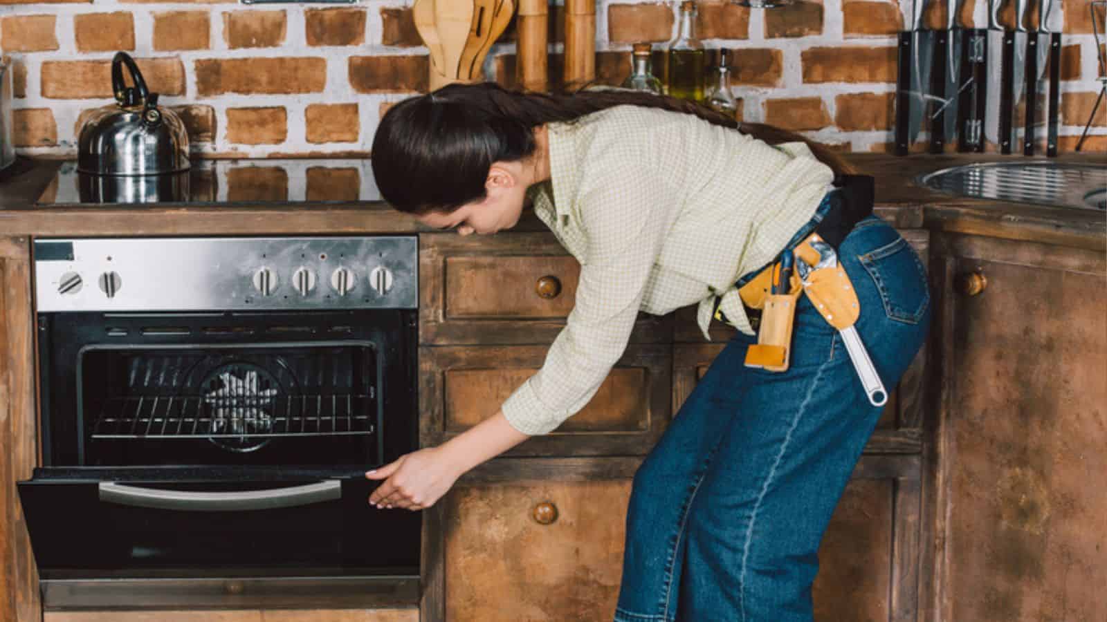 Confident young repairwoman examining oven at kitchen