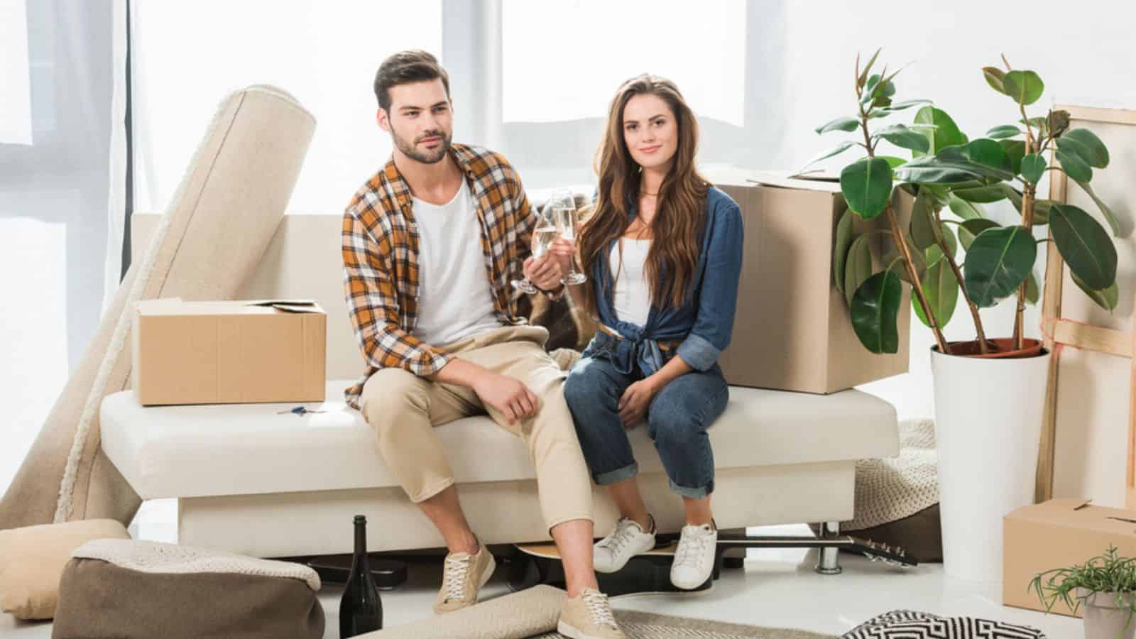 Couple in love clinking glasses of champagne at new house with cardboard