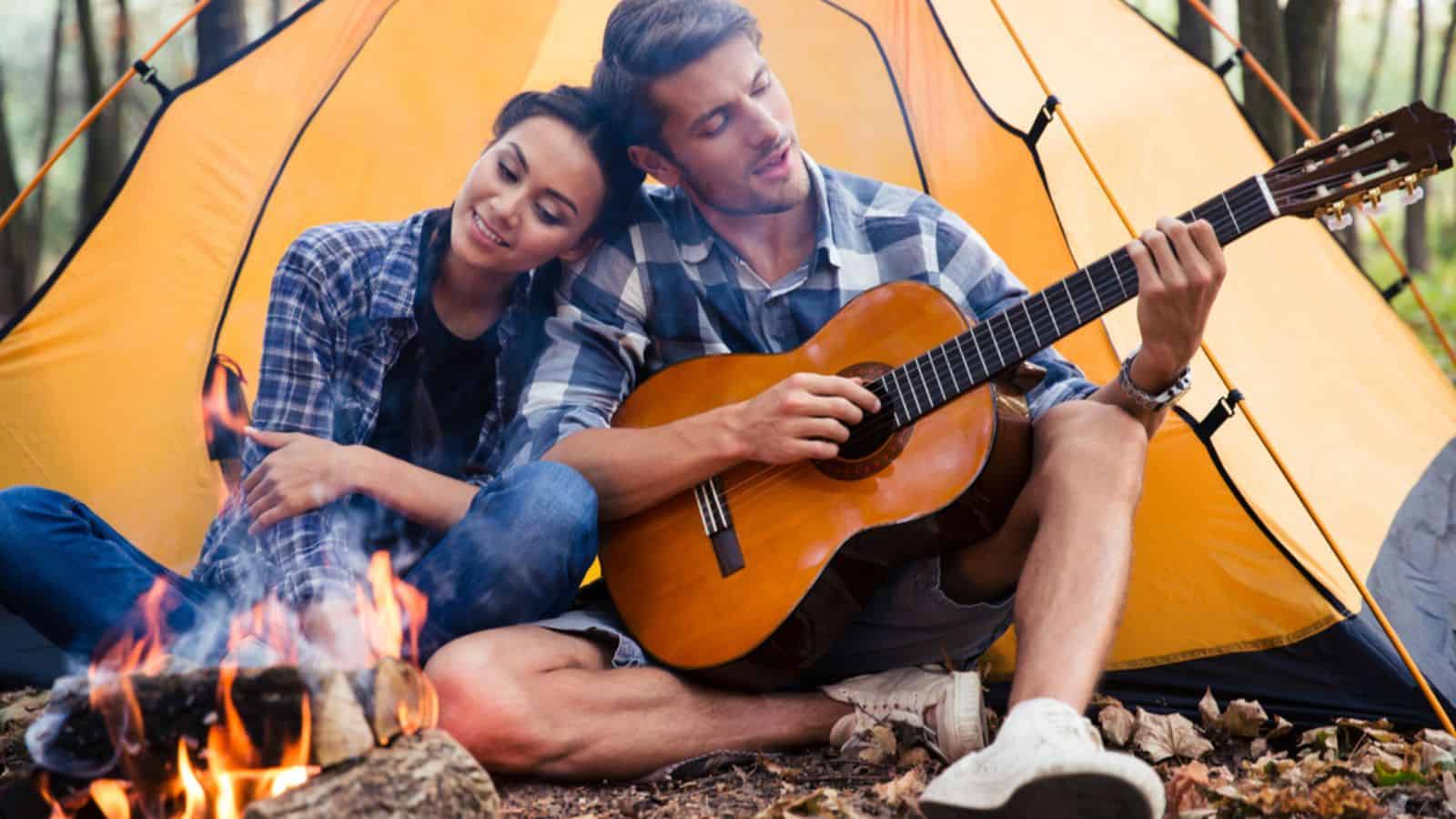 Couple sitting with guitar near bonfire for caping
