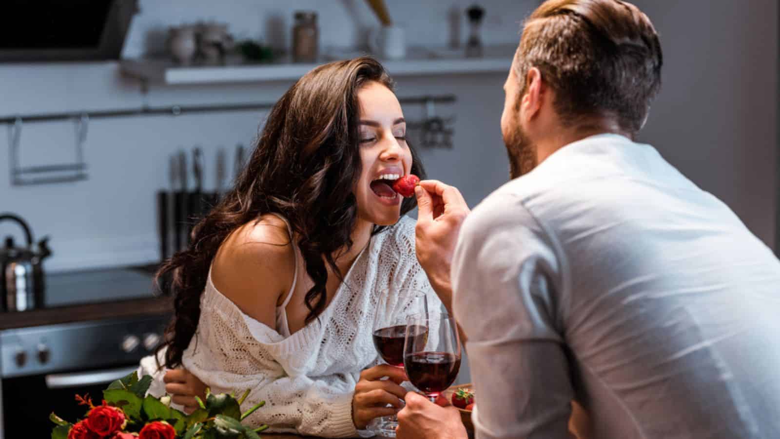 Couple with glasses of red wine at wooden table with bouquet of roses