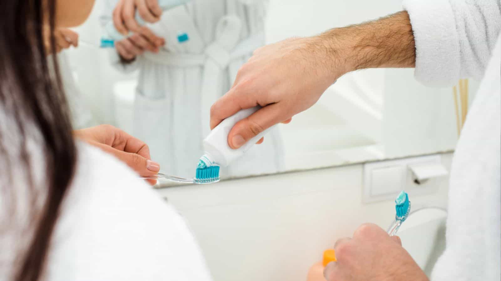 Cropped view of man adding toothpaste on woman toothbrush