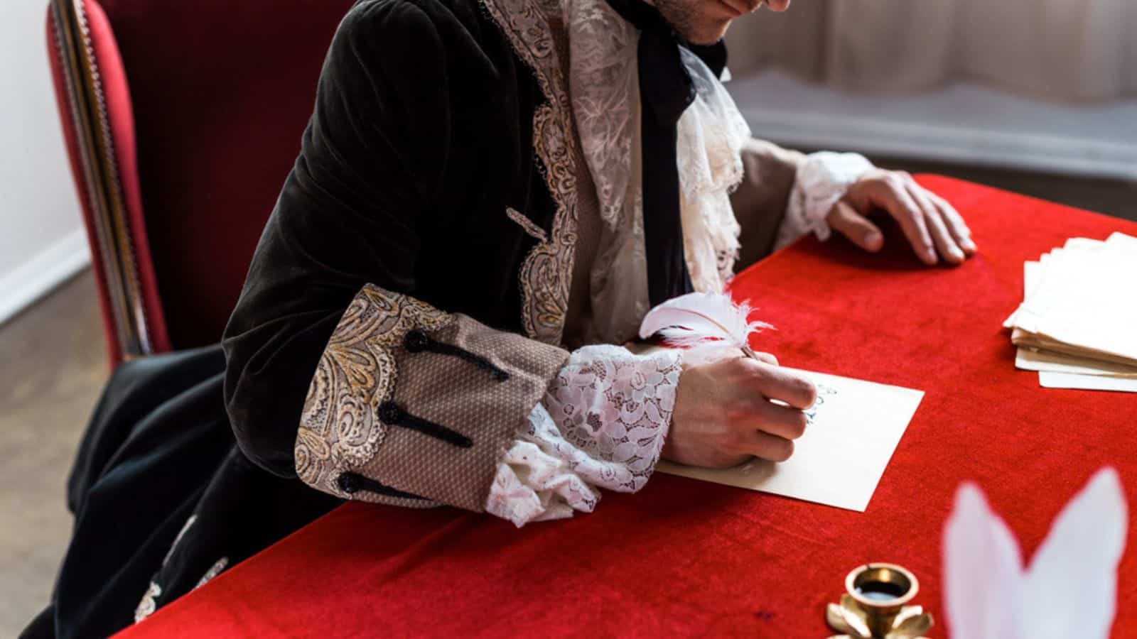 Cropped view of victorian man holding feather and writing letter