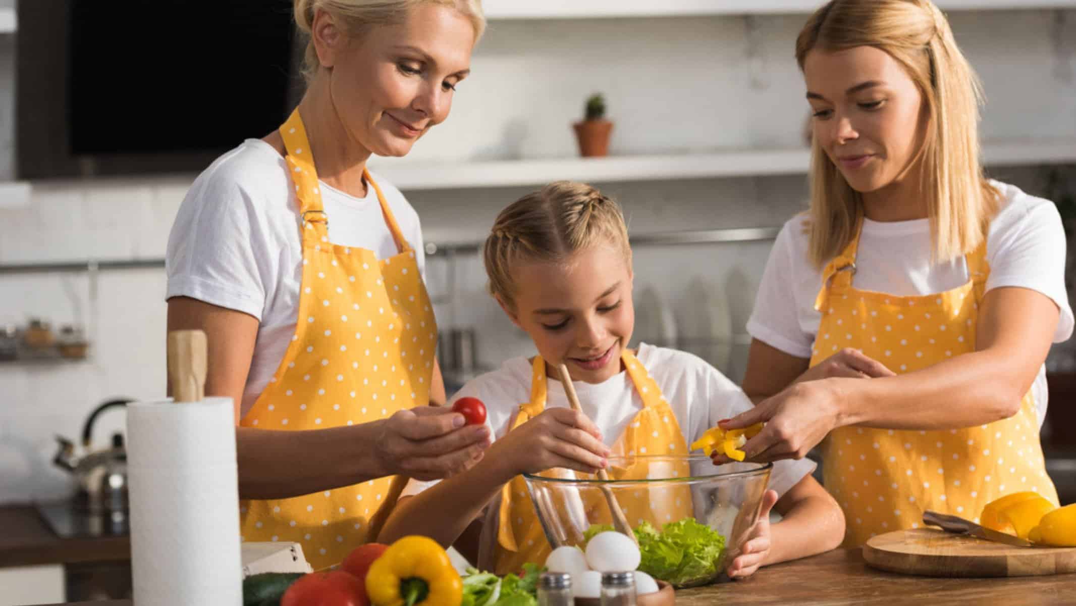 Cute happy child with mother and grandmother cooking vegetable salad
