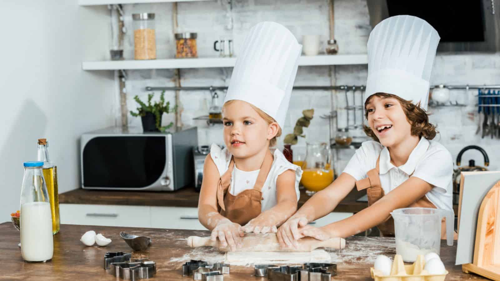 Cute happy children in chef hats preparing dough for cookies