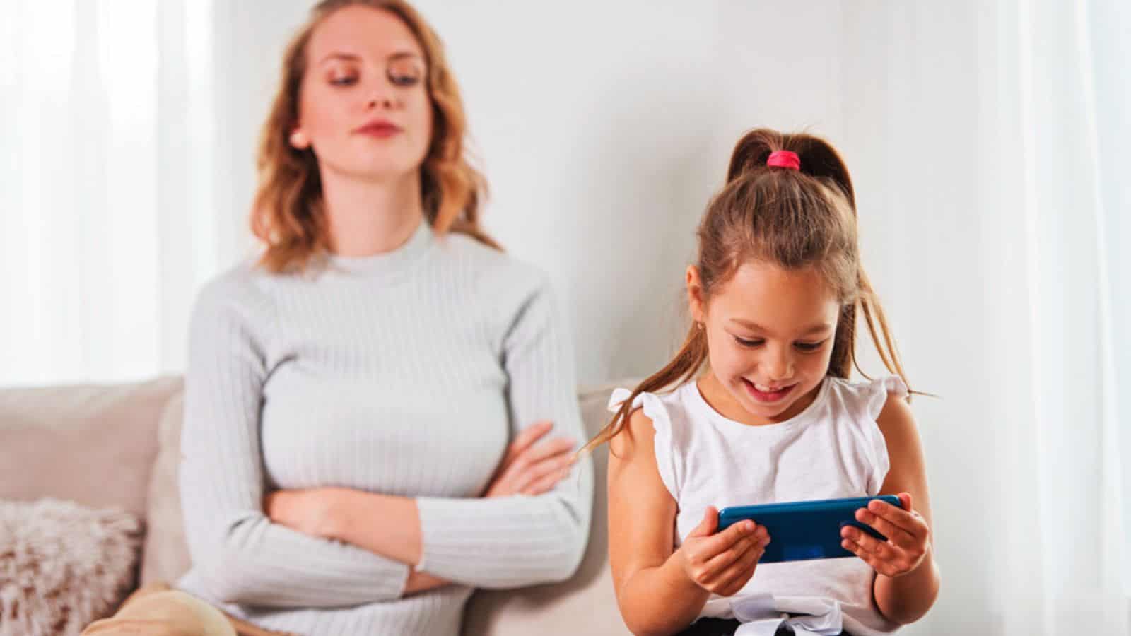 Daughter using a smartphone, while frustrated mother is watching her