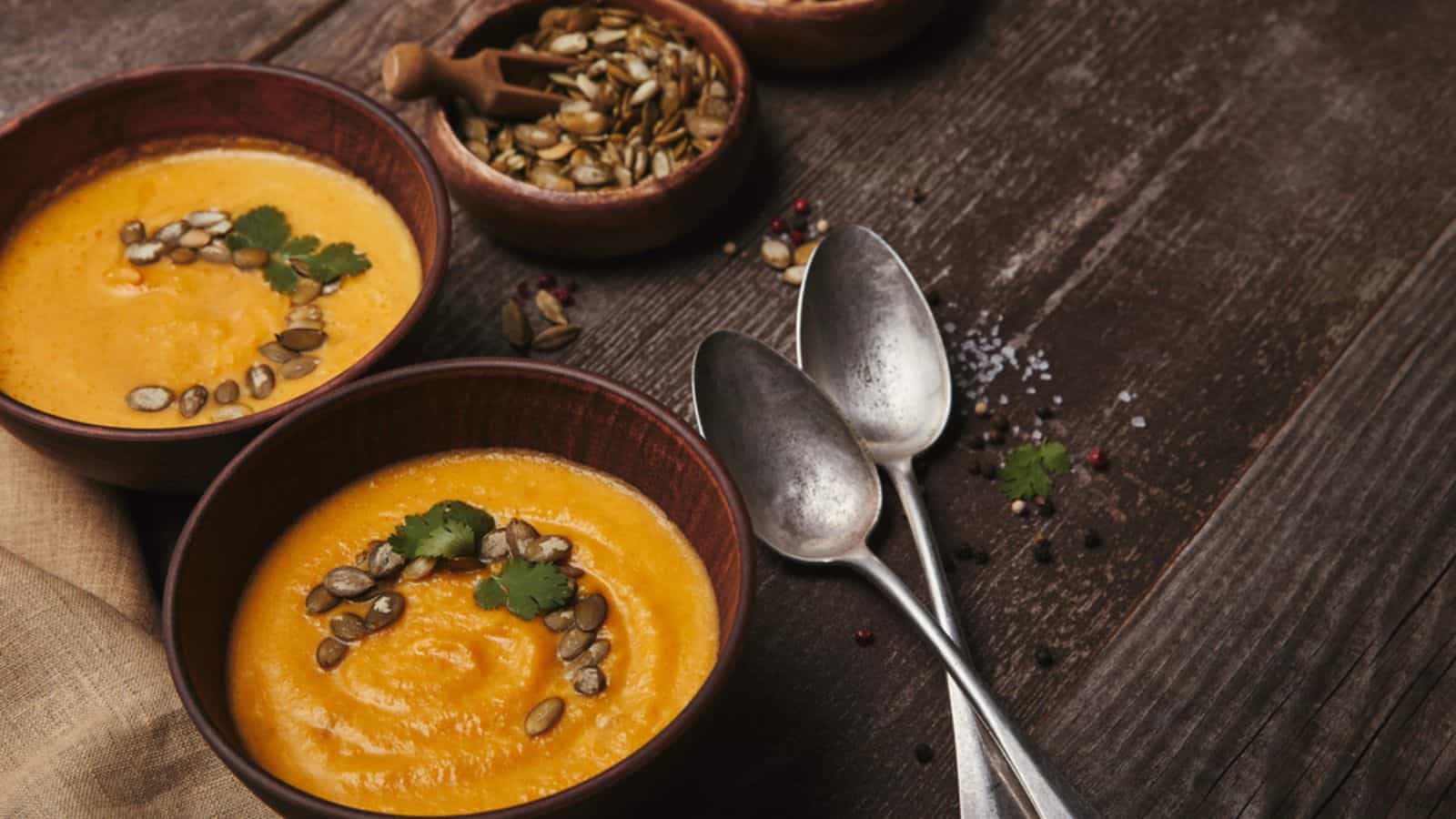 Delicious pumpkin soup in bowls and spoons on wooden table