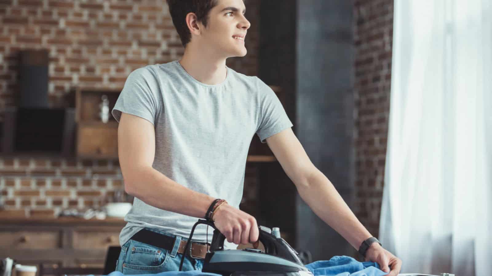 Dreamy caucasian teenager ironing blue shirt at home