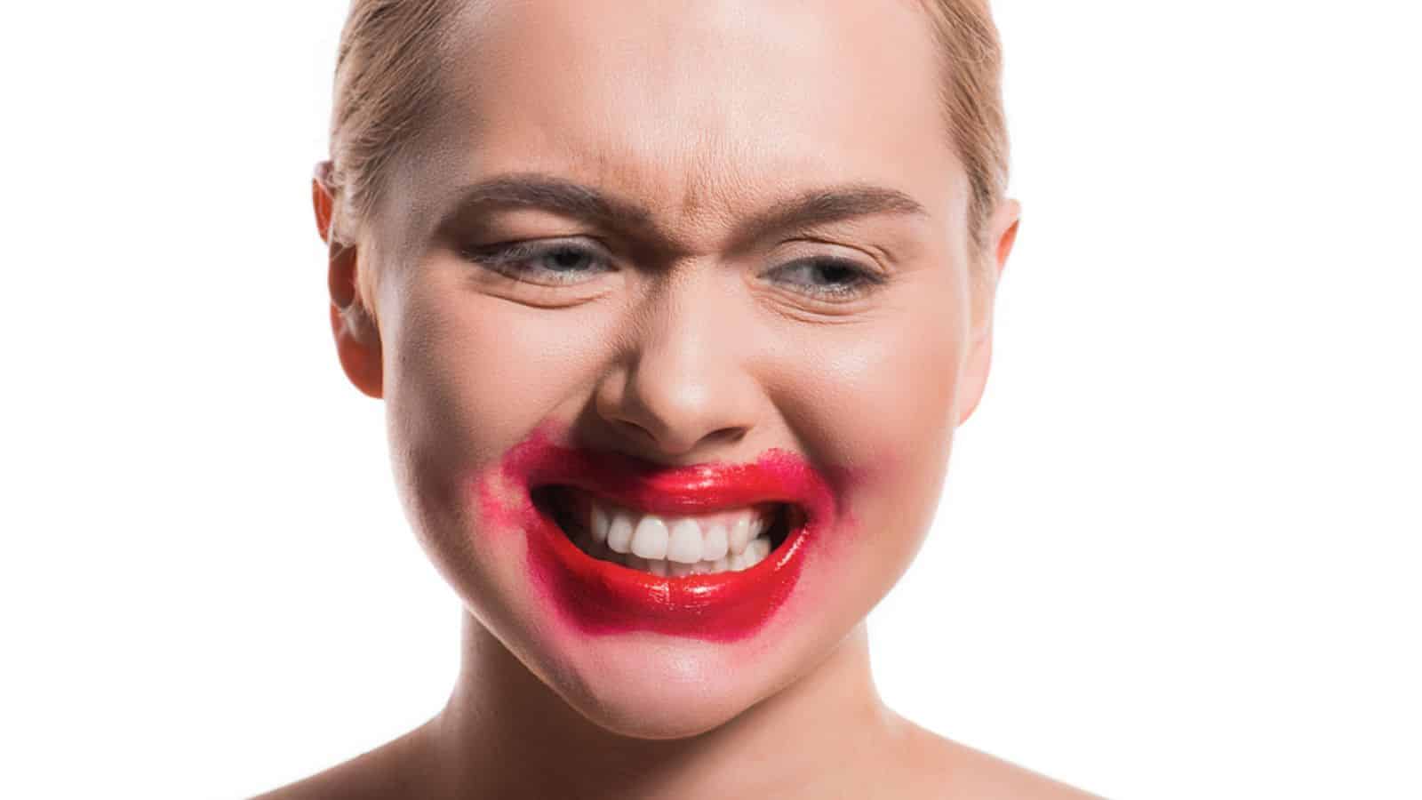 Emotional woman with smeared red lipstick on face