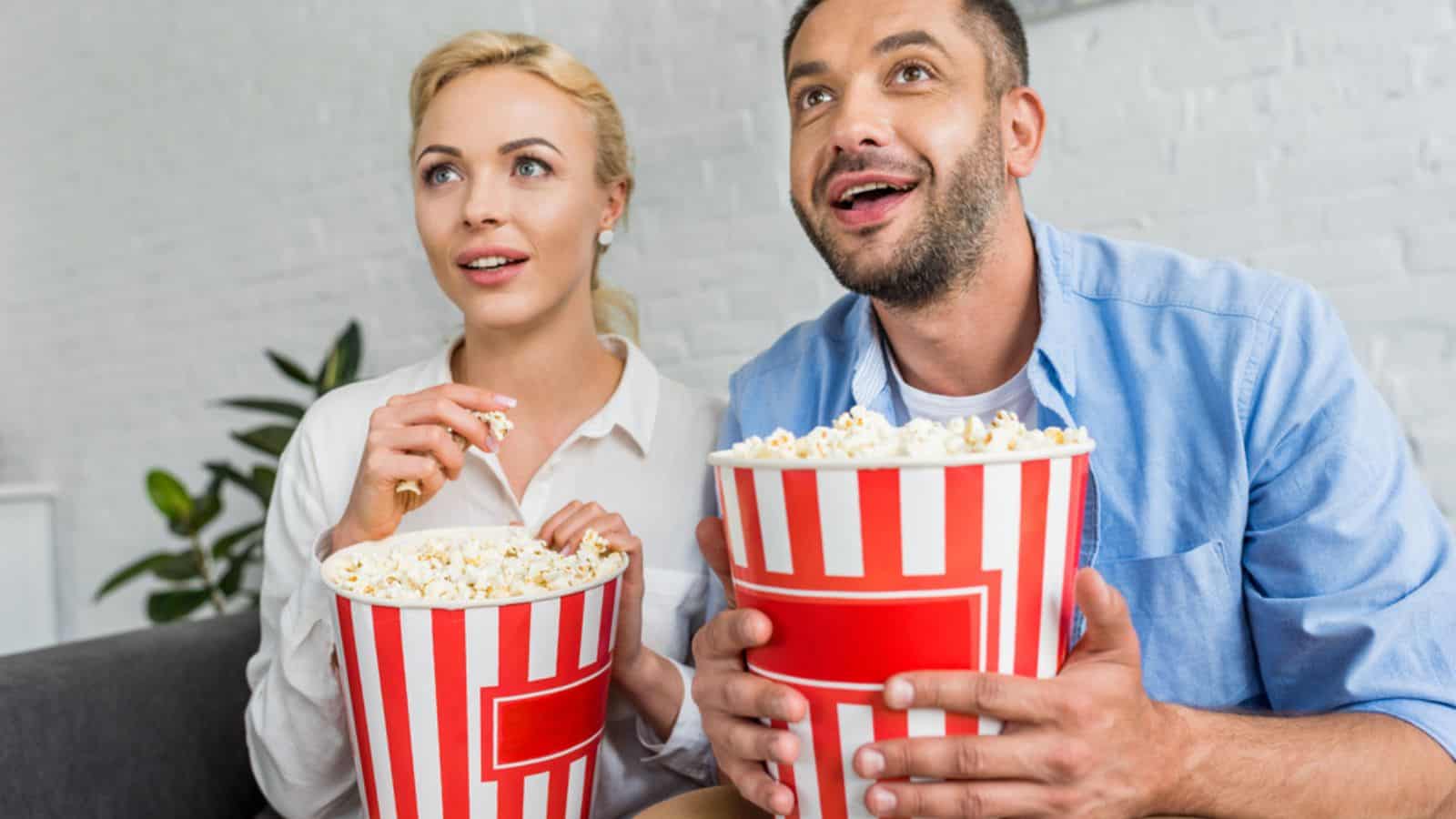 Excited couple eating popcorn and looking away at home