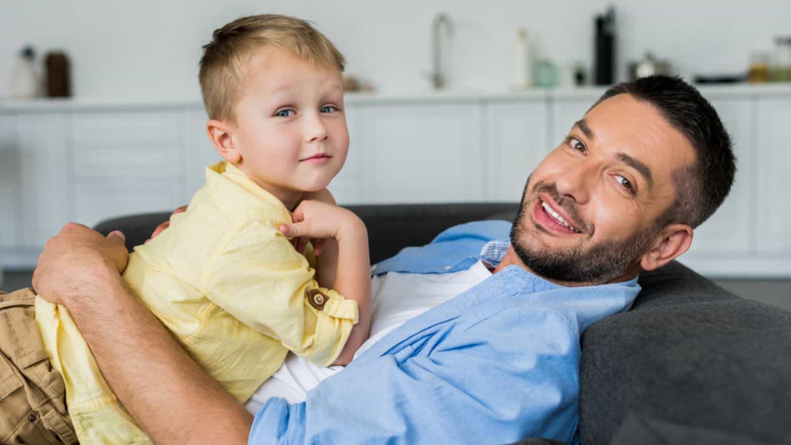 Father with cute little son lying on sofa and smiling