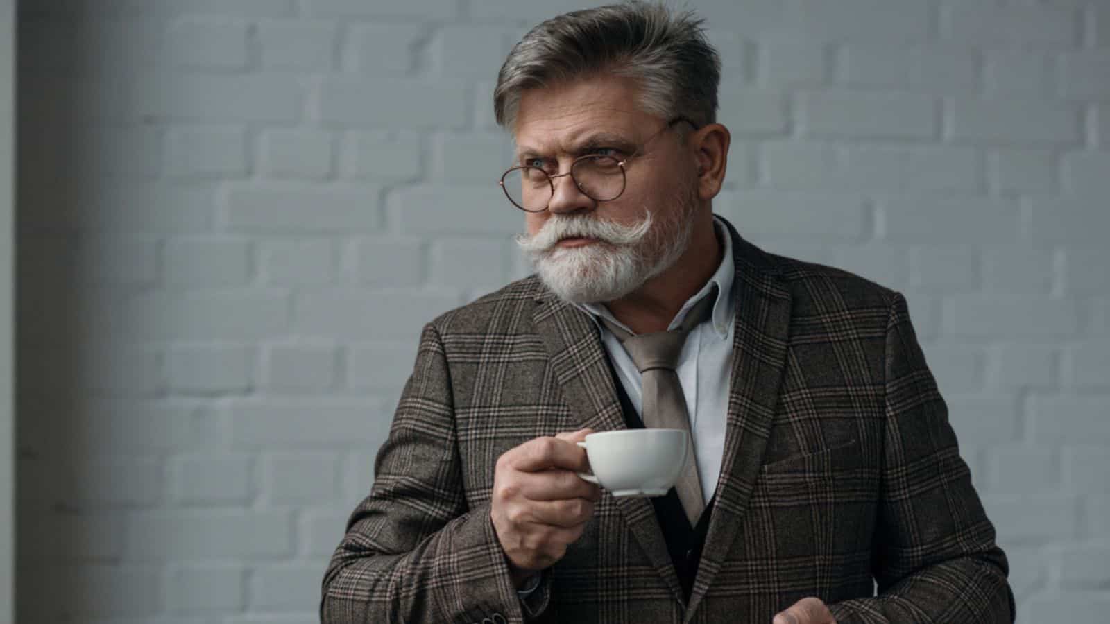 Handsome senior man with cup of coffee in front of white brick