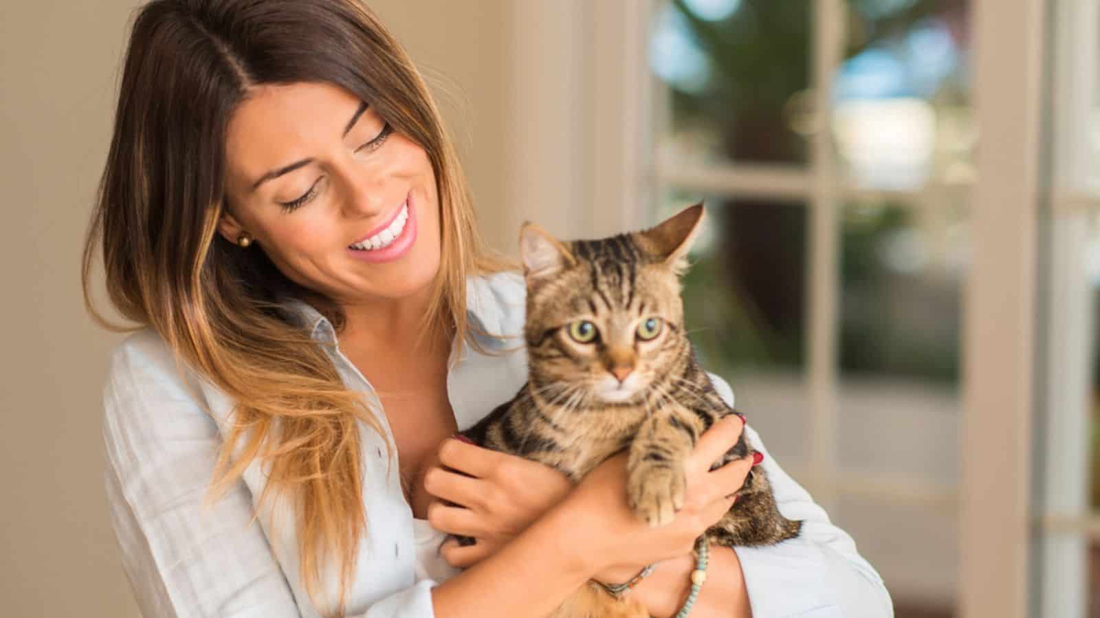 Happy beautiful woman smiling and cuddling cat with love at home