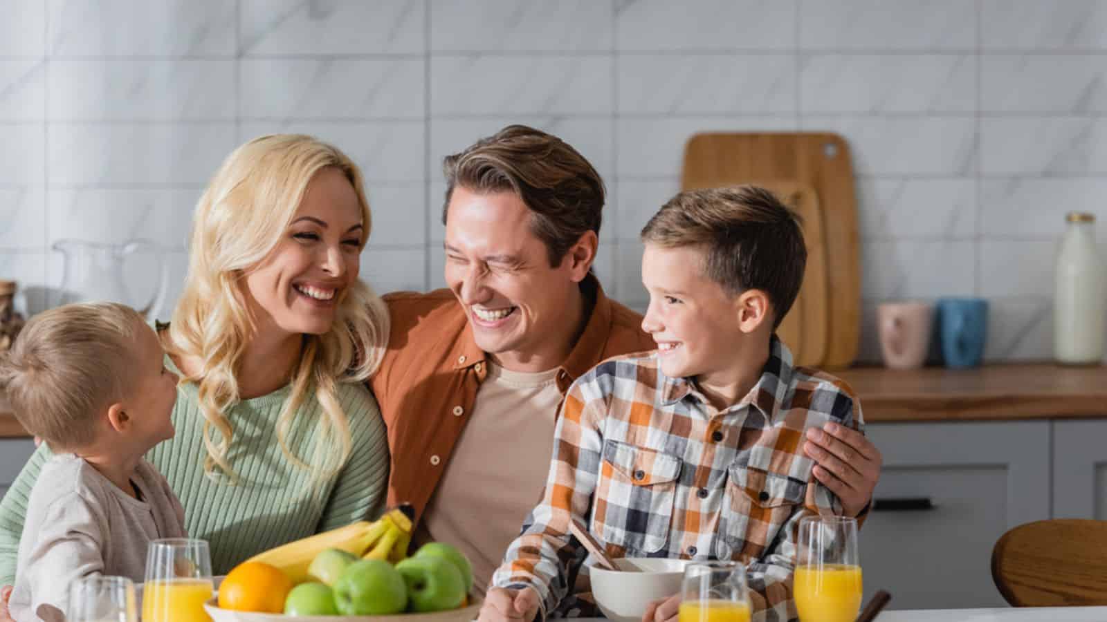 Happy family laughing in kitchen near glasses with orange juice
