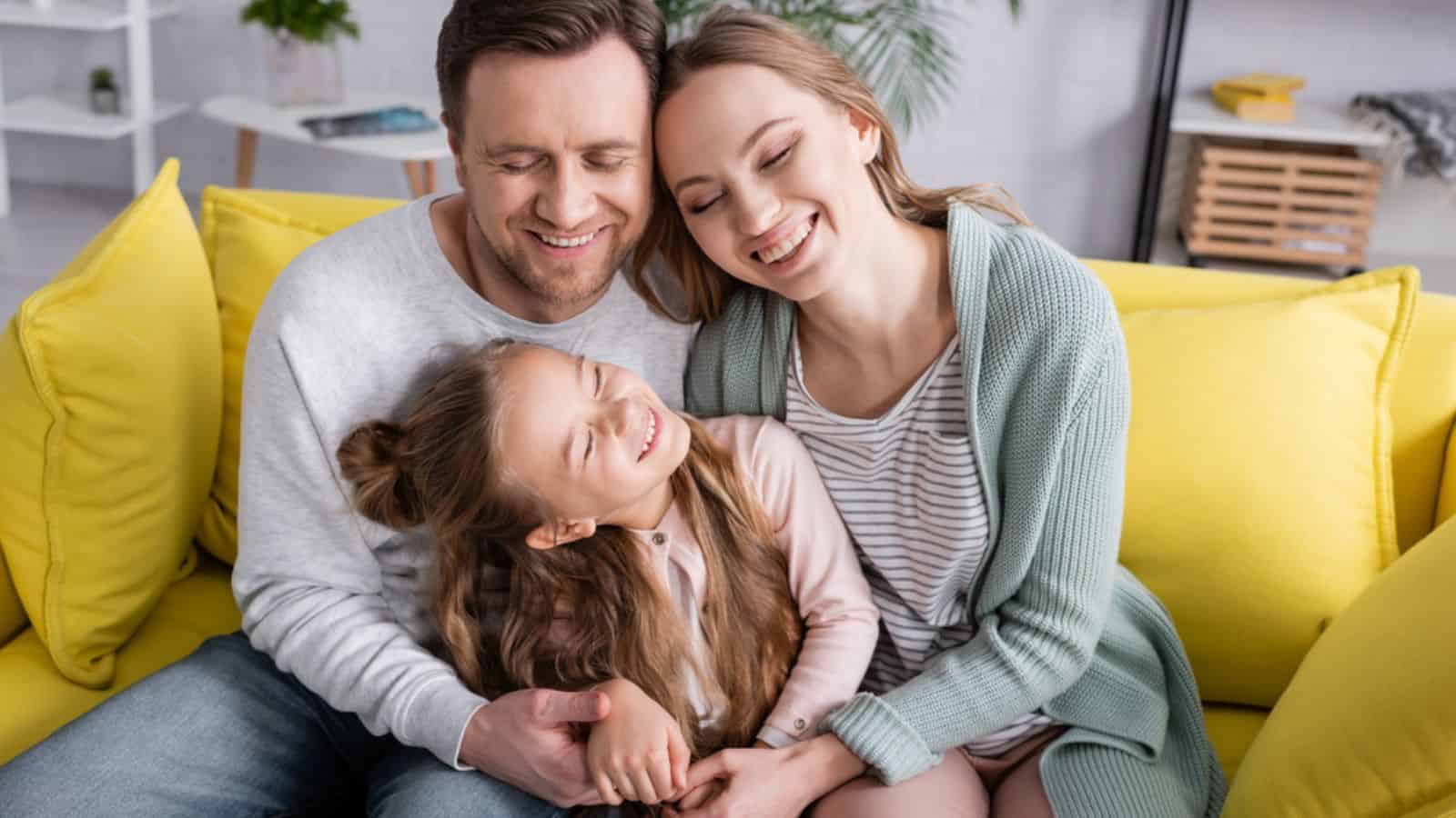 Happy family with closed eyes hugging on couch