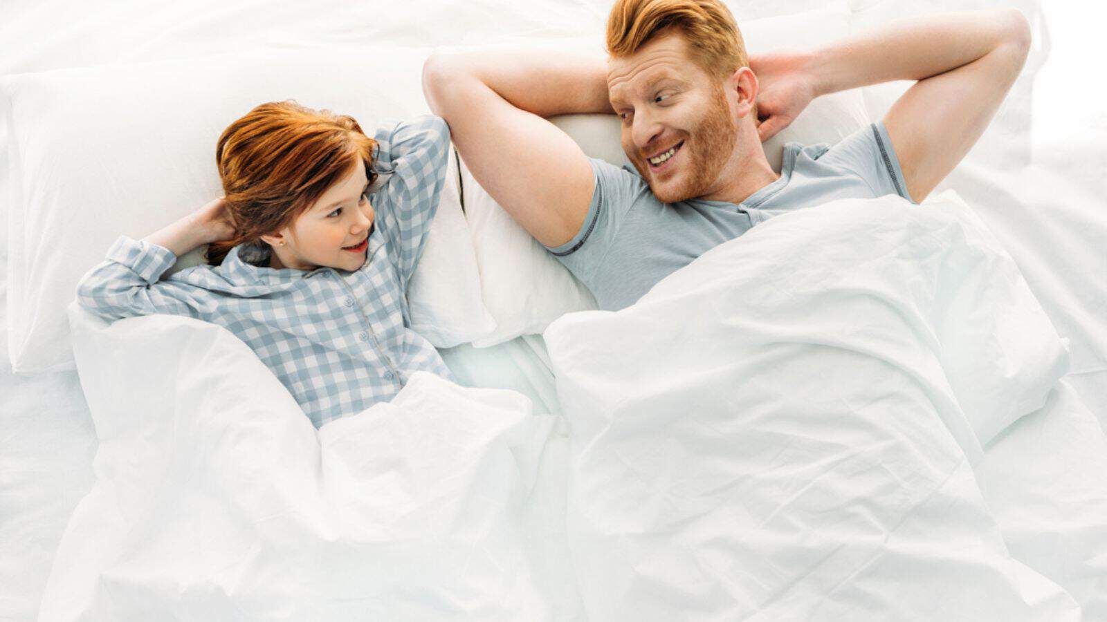 Happy father and daughter lying together in bed and smiling each other