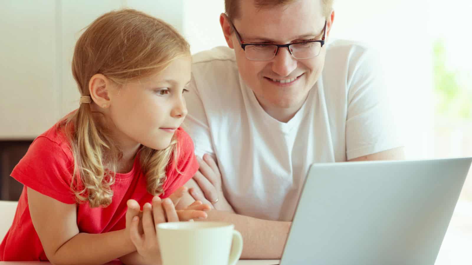 Happy young father with cute daughter learning together online using laptop at home