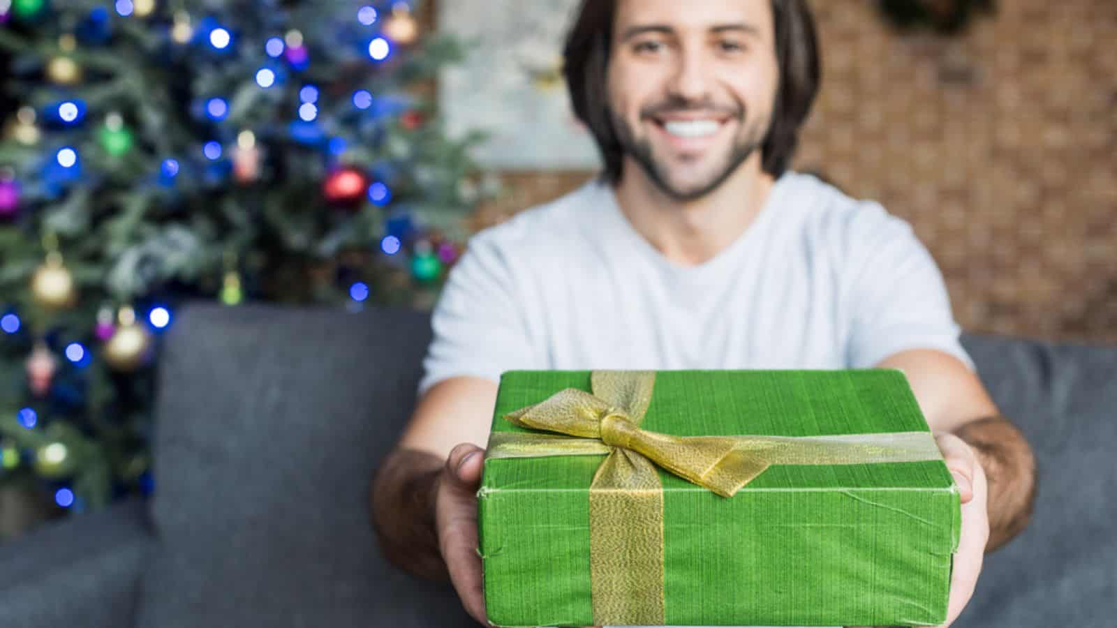 Happy young man holding christmas present and smiling