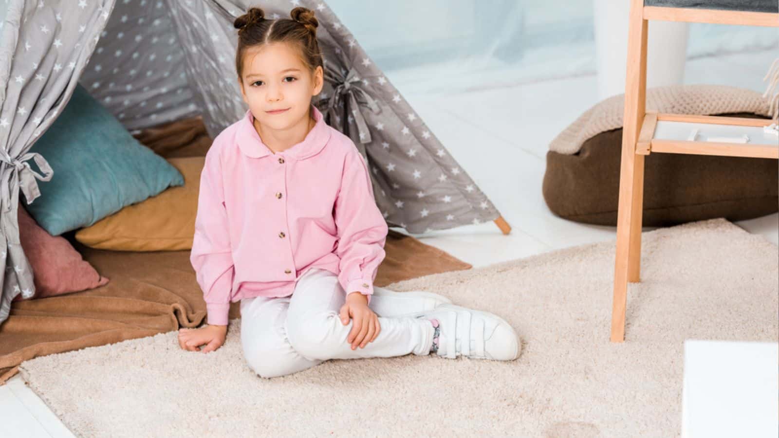 High angle view of adorable little girl sitting on carpet and smiling at camera