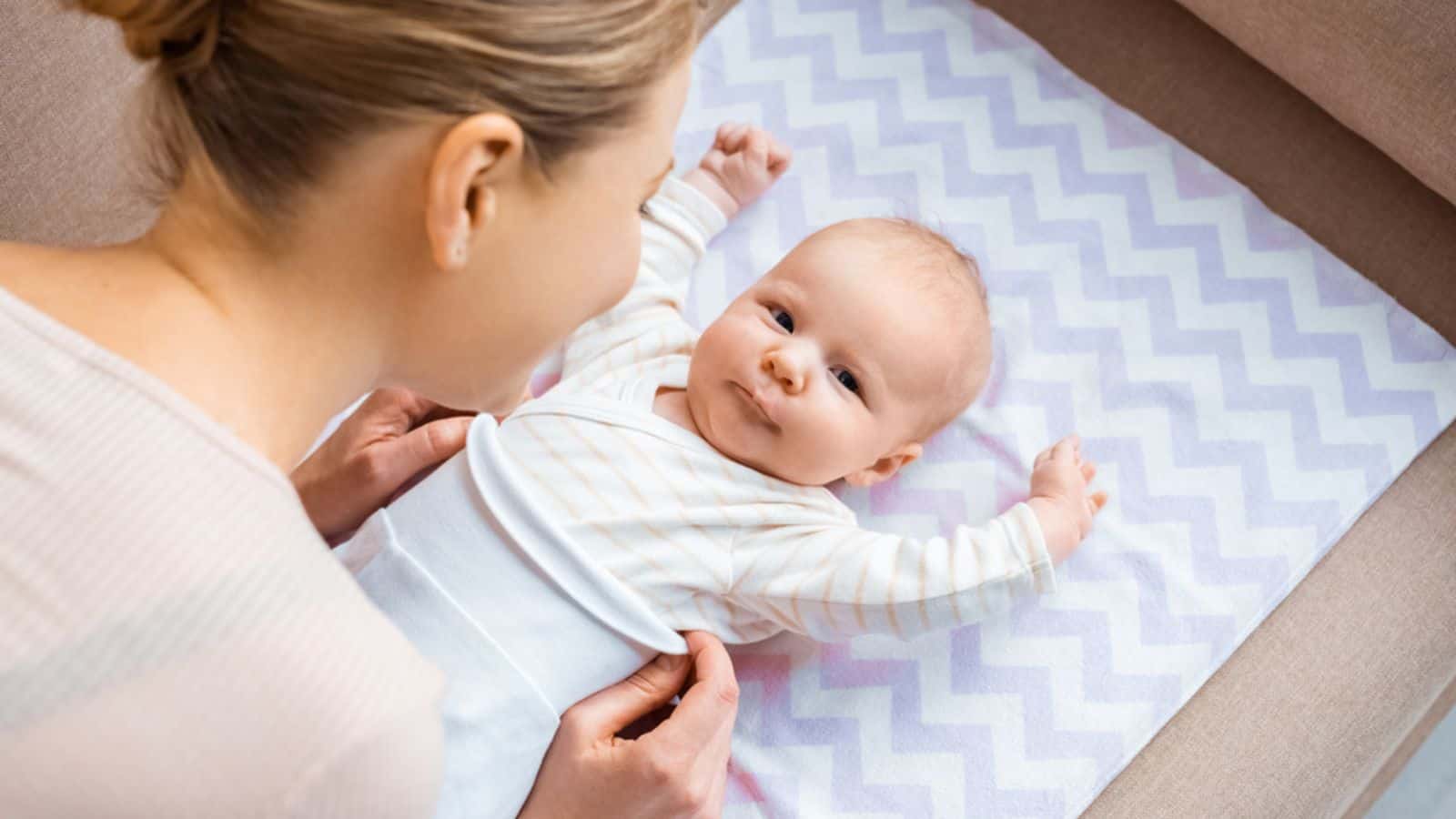 High angle view of mother putting clothes on adorable infant baby