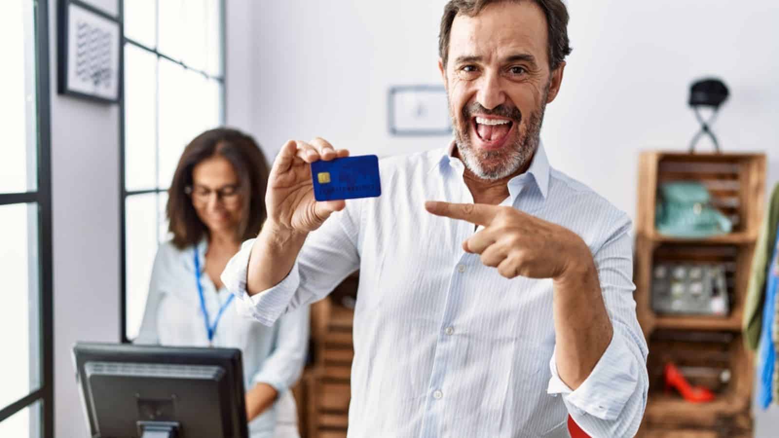 Hispanic man holding credit card at retail shop smiling happy pointing with hand finger