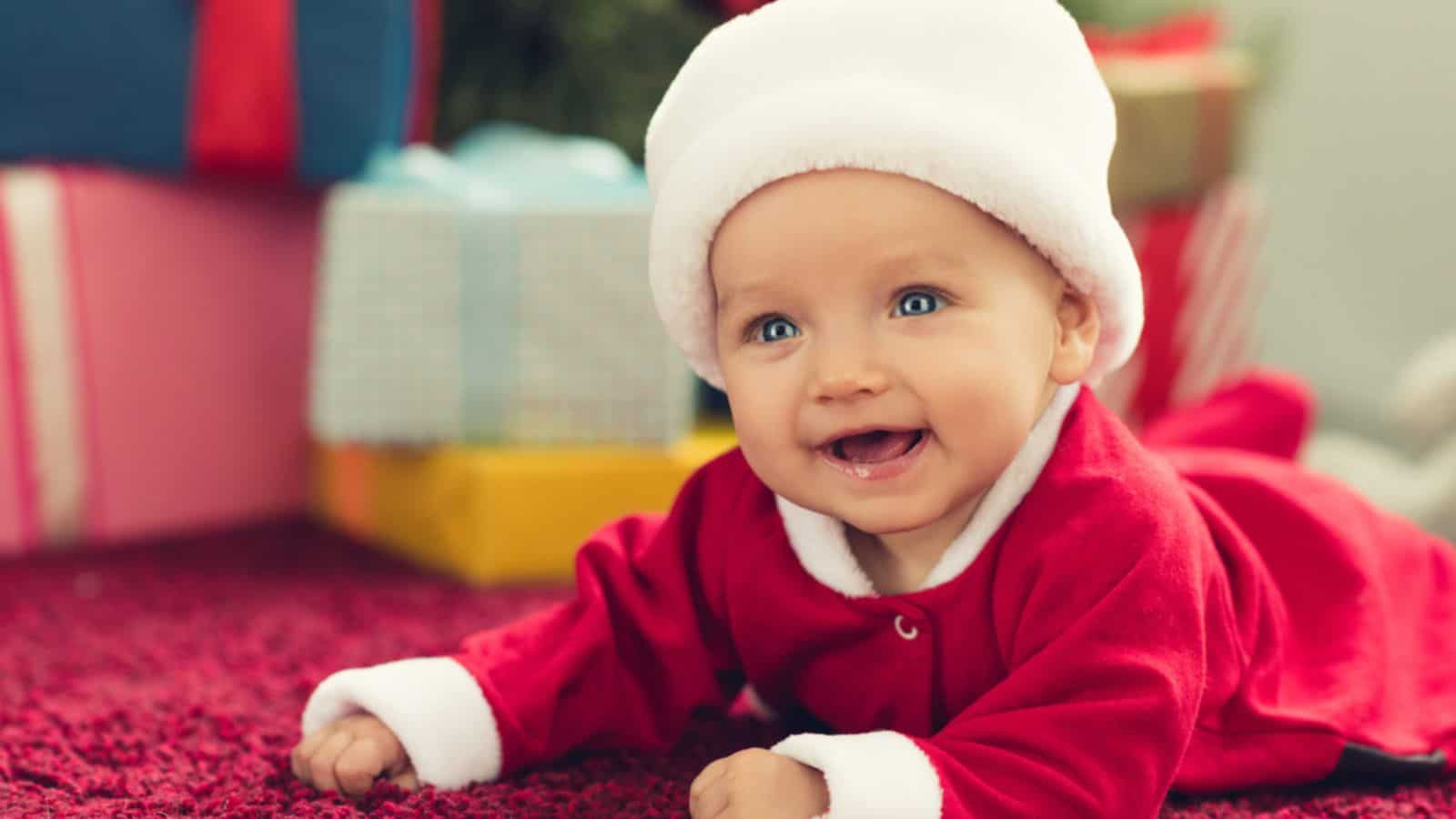 Laughing little baby in santa suit lying on red carpet