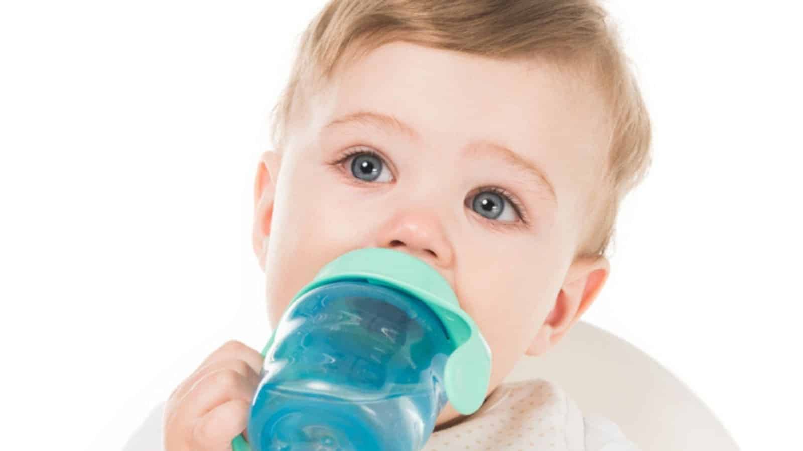 Little boy drinking water from baby cup in highchair