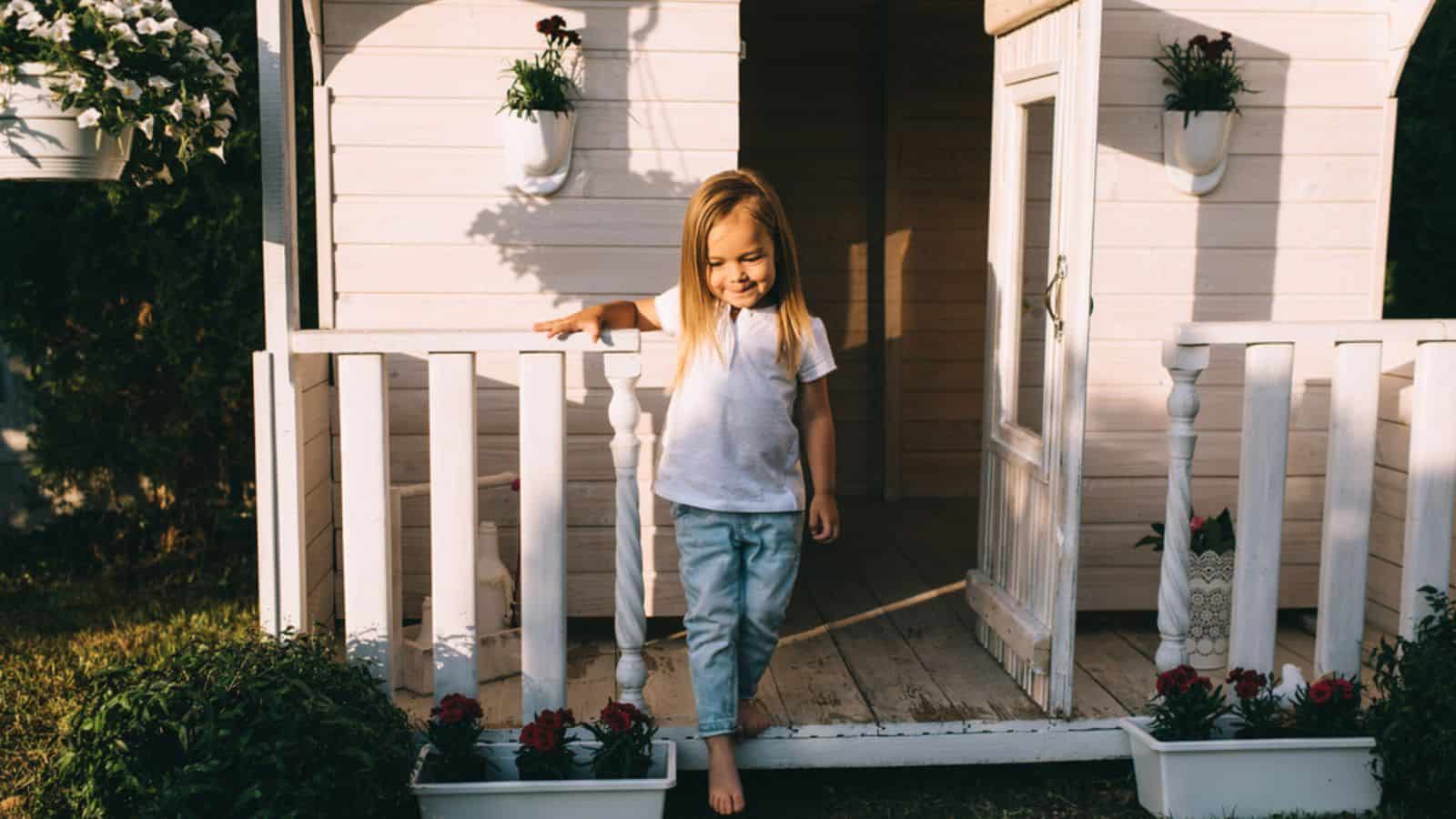Little kid standing on porch of country house alone on summer day