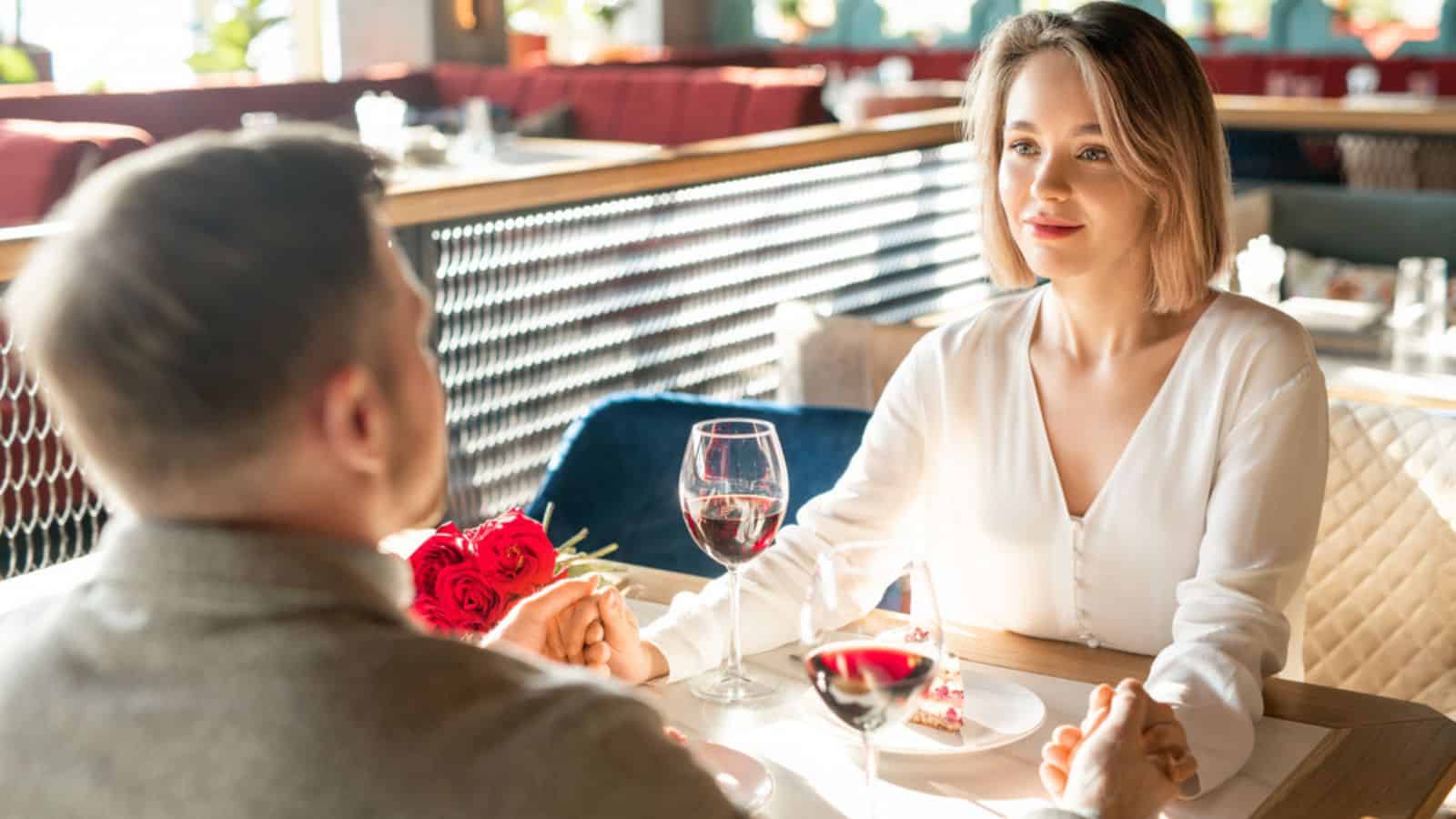 Lovey-dovey man and woman sitting in front of each other at restaurant table gently holding hands and looking at each other