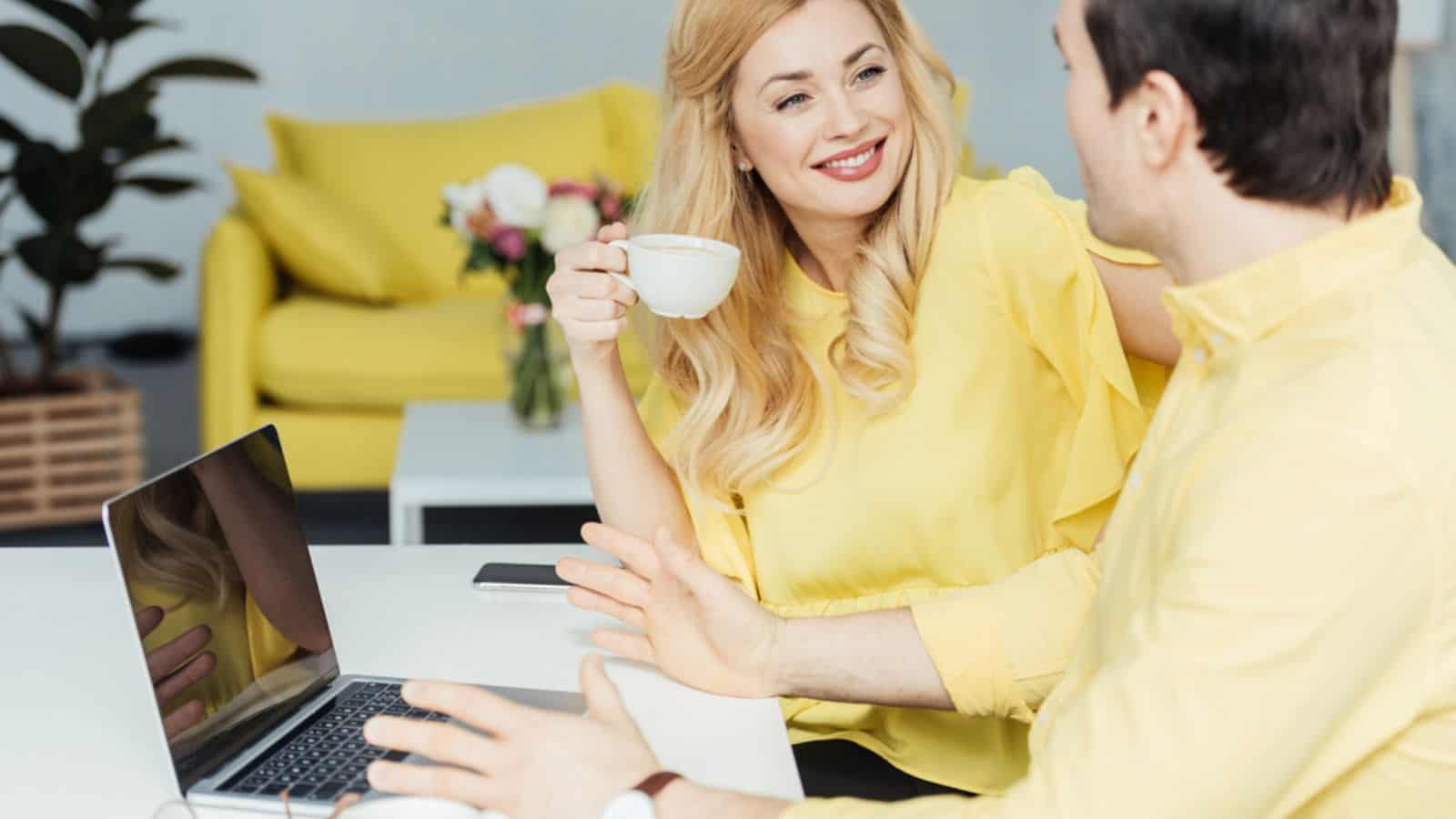 Man and woman drinking coffee and working by laptop in kitchen