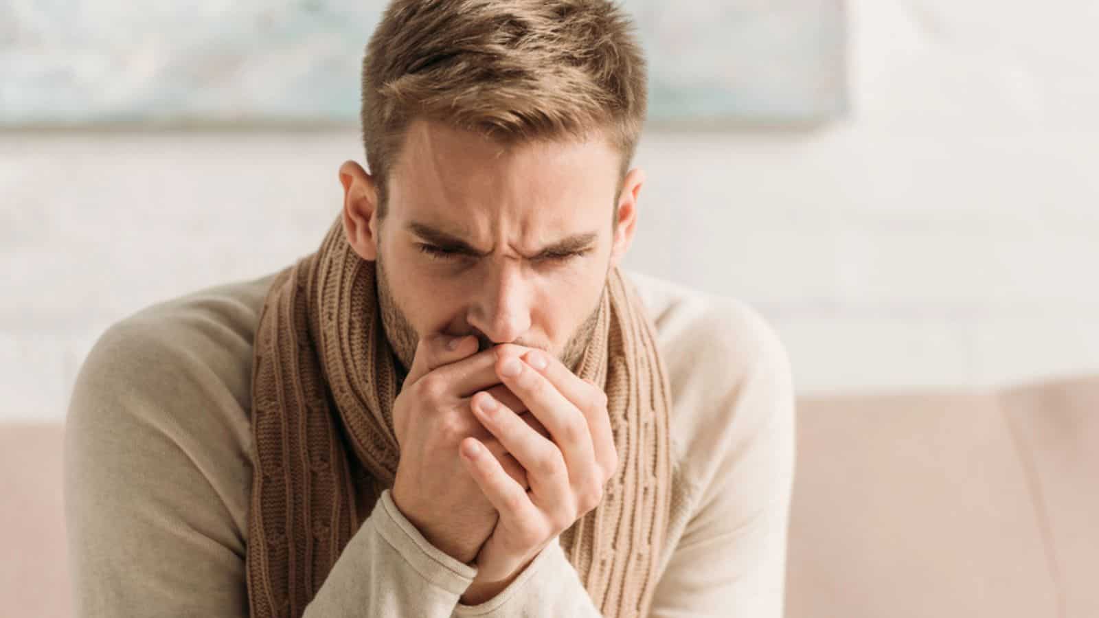 Man in warm scarf coughing in folded hands