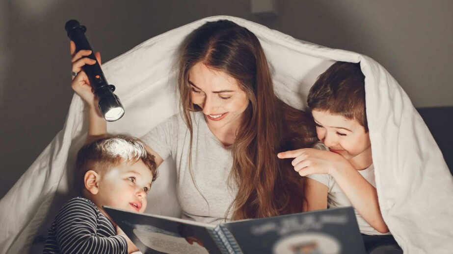 Mom and her kids reading a book with a flashlight
