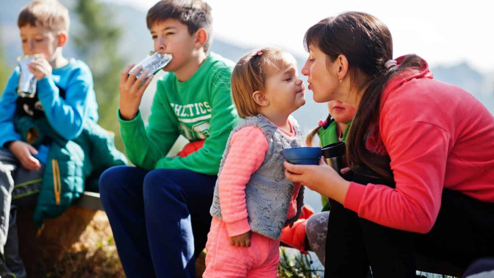 Mother with four kids resting and eating snacks in mountains. Travel and hiking with childrens.