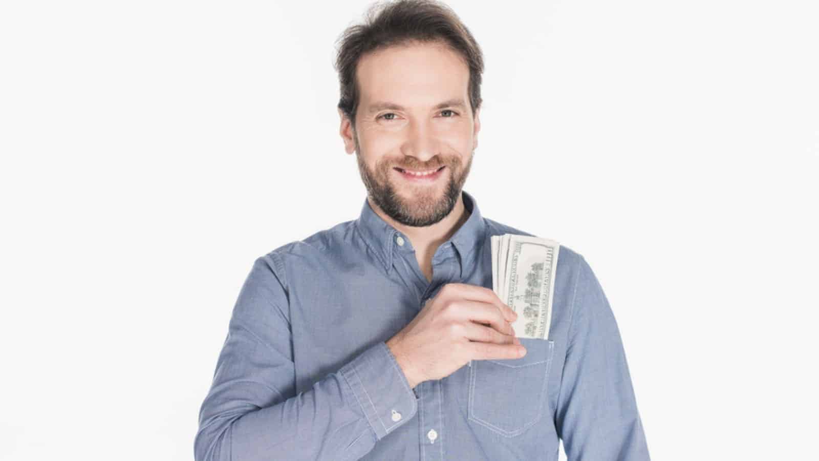 Portrait of cheerful bearded man with dollar banknotes in pocket
