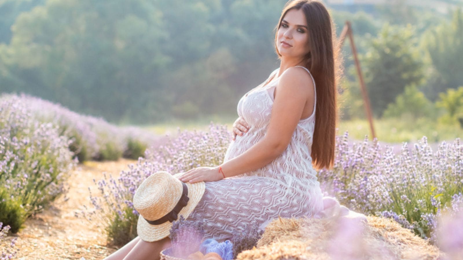 Pregnant woman wearing maternity dress in violet lavender field looking at camera