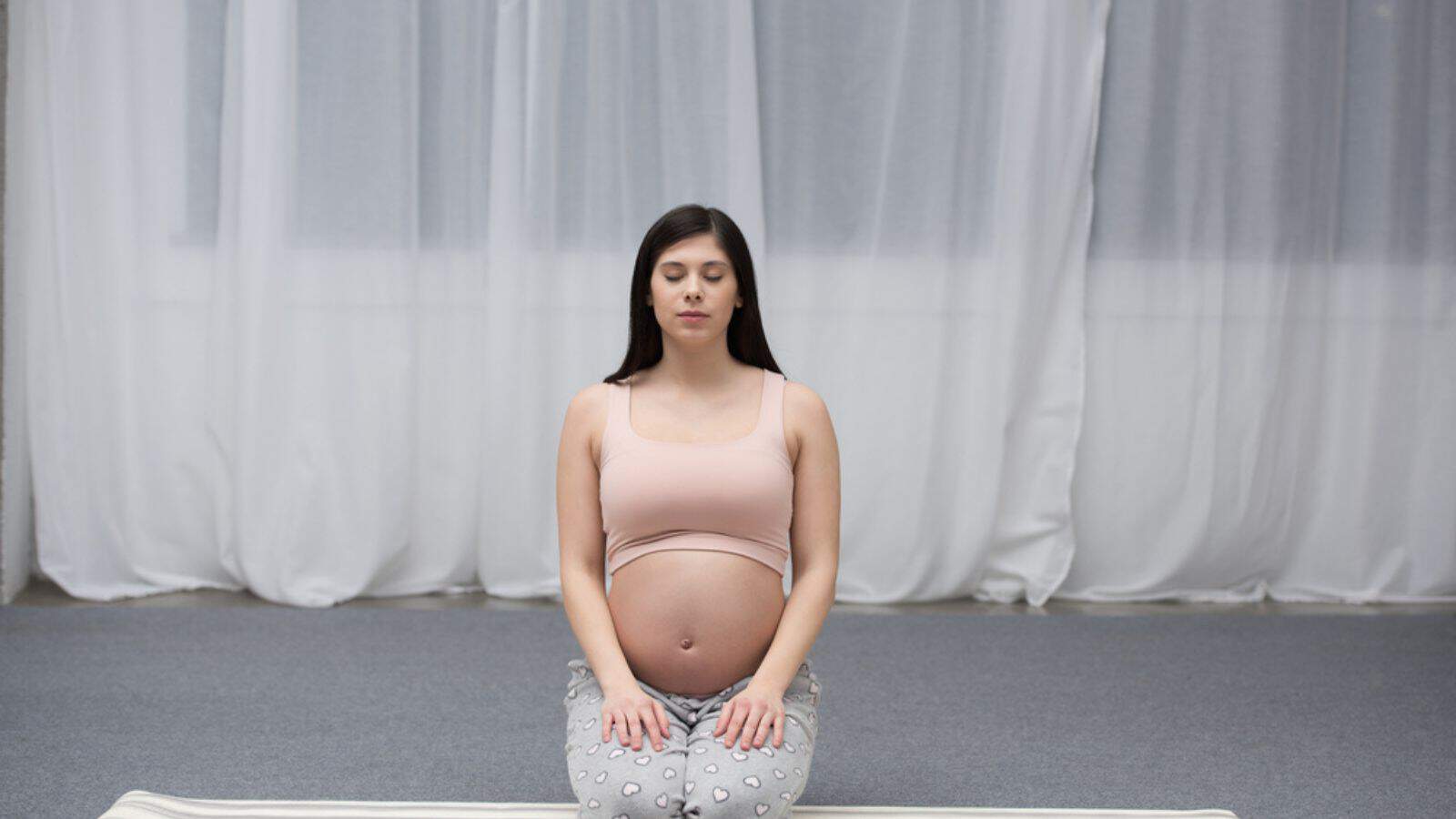 Pregnant young woman with closed eyes sitting on yoga mat